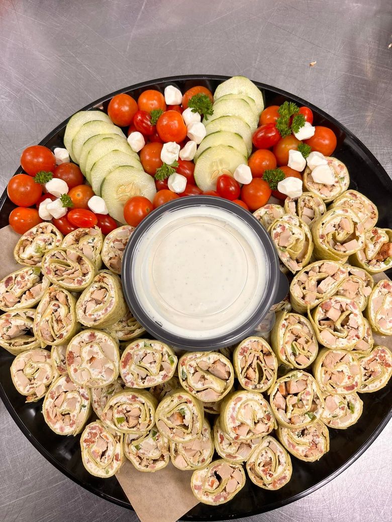 Appetizer platter with chicken wraps, vegetables, and dip.