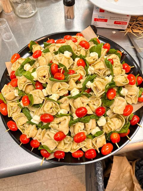 Tortellini skewers with cherry tomatoes and mozzarella on a black platter.