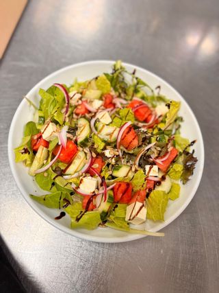 Salad with tomatoes, cucumber, onions, cheese, and balsamic glaze on a white plate.
