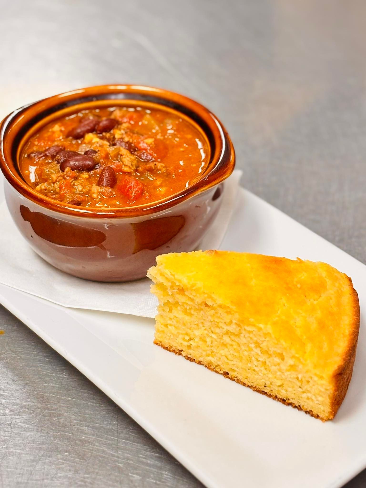 Chili in a brown bowl with a slice of cornbread on a white plate.