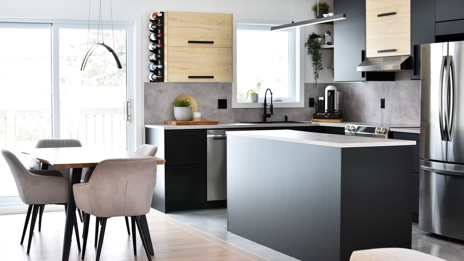 Cuisine moderne avec placards noirs et en bois, îlot central, table à manger et réfrigérateur en acier inoxydable.