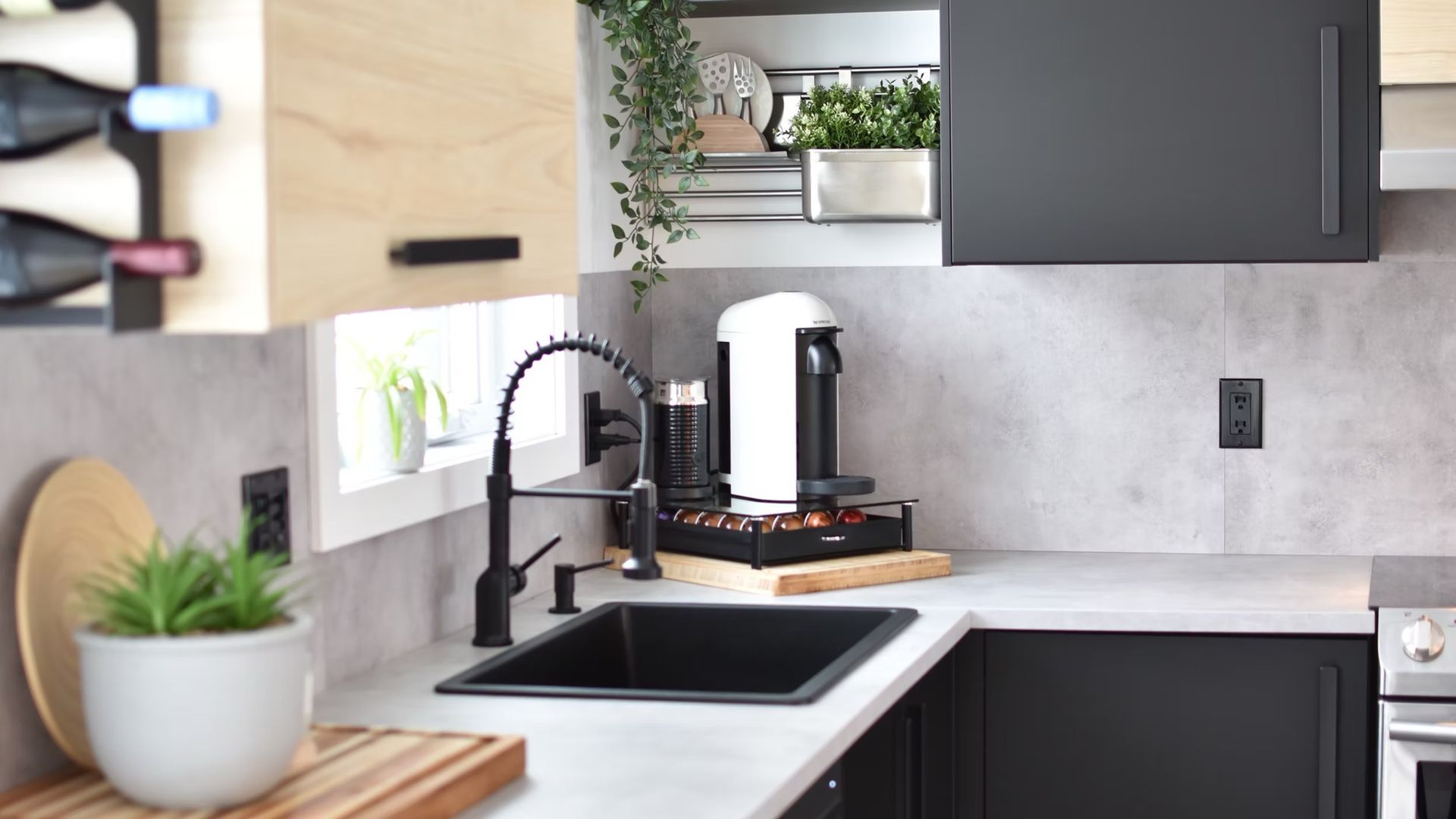 Coin cuisine moderne avec évier et robinet noirs, machine à expresso, comptoirs gris et armoires noires.
