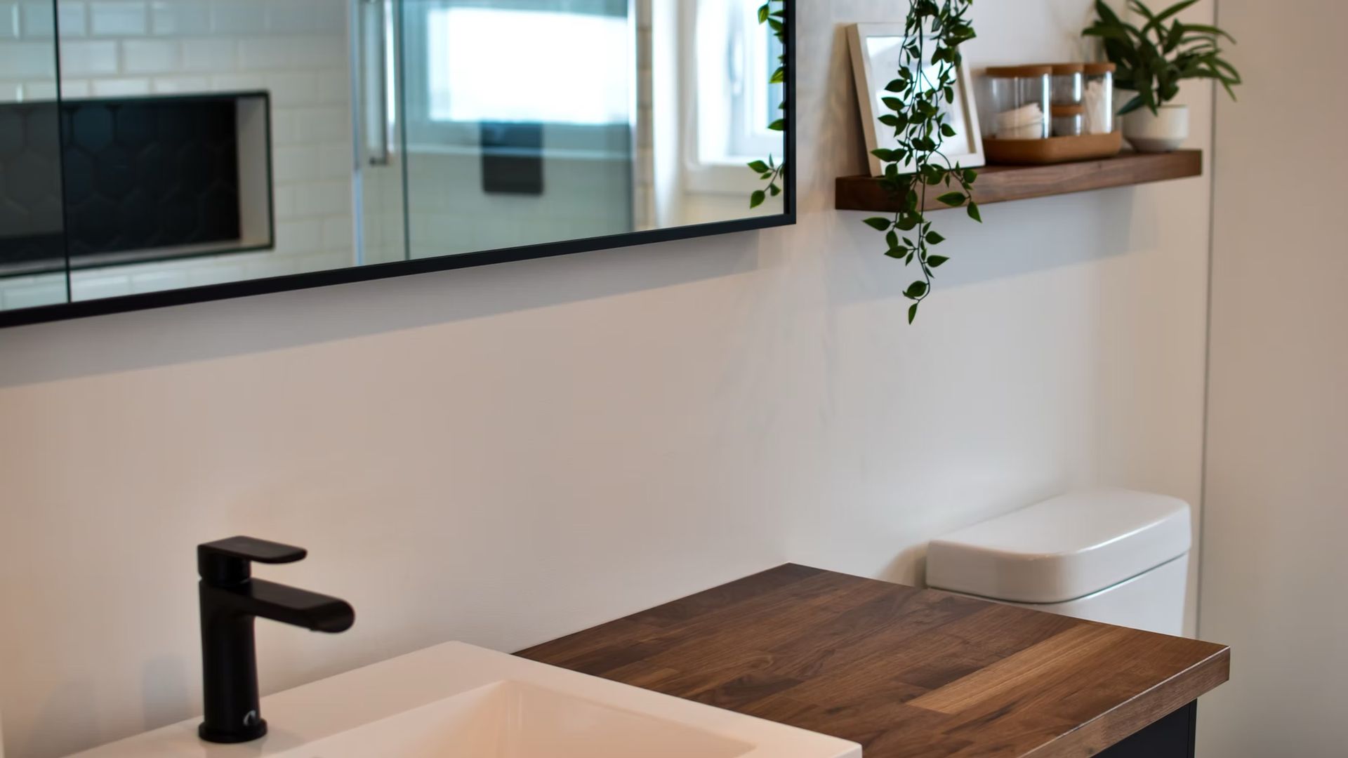 Salle de bains moderne avec robinet noir, comptoir en bois et étagère décorative.