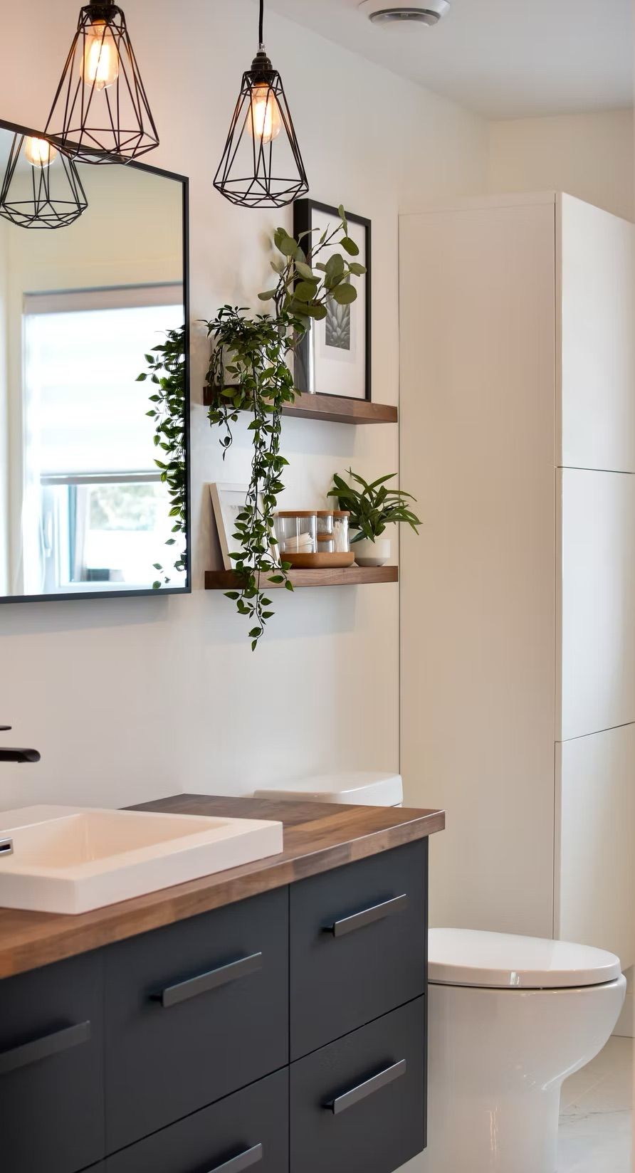 Salle de bains moderne avec meuble-lavabo noir, toilettes blanches et plantes suspendues.