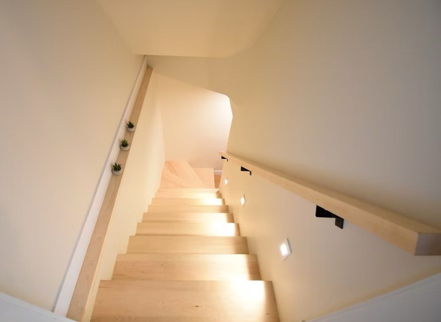 Escalier avec marches et rampe en bois clair, éclairage intégré et murs blanc cassé.