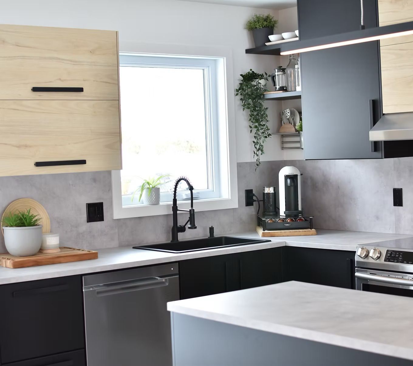 Cuisine moderne avec placards en bois noir et clair, appareils électroménagers en acier inoxydable et une fenêtre.