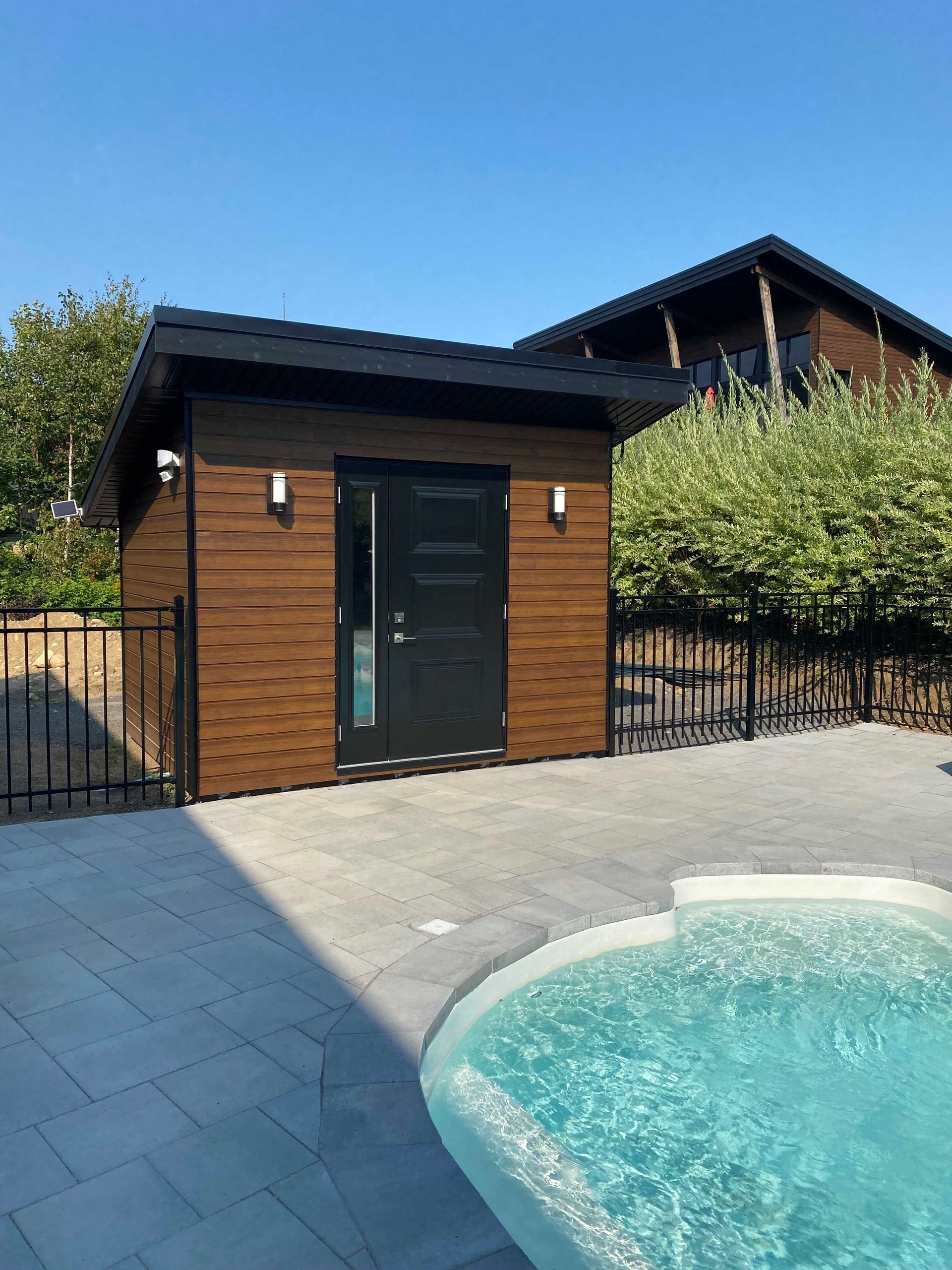 Petit cabanon marron avec une porte noire, à côté d'une piscine.