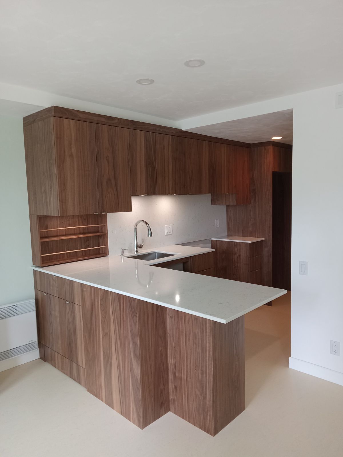 Cuisine moderne avec placards en bois foncé, plans de travail blancs et évier.