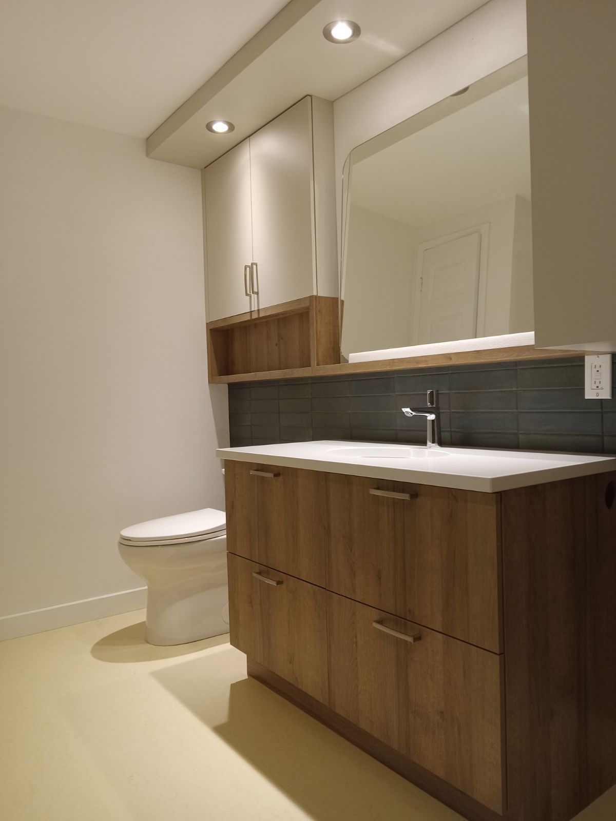 Salle de bains moderne avec meuble-lavabo en bois, toilettes blanches et grand miroir.