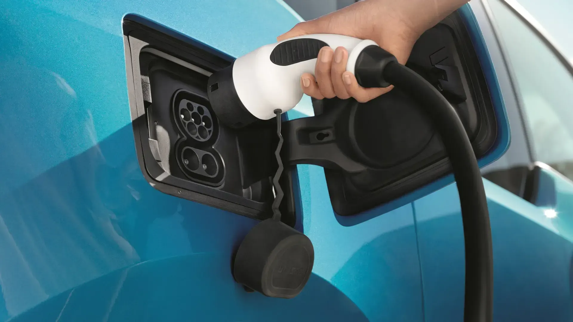 Hand plugging an electric vehicle into a blue car’s charging port