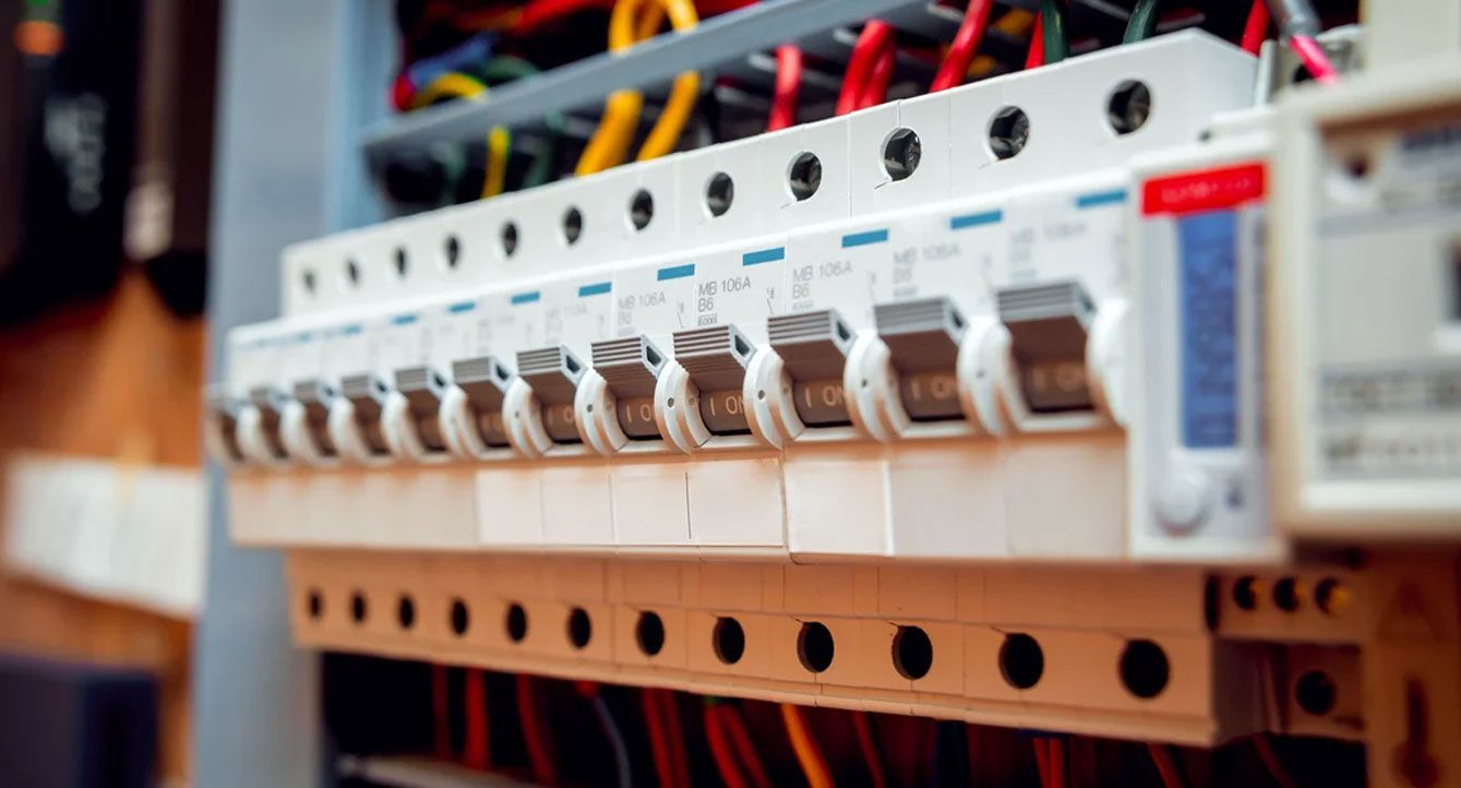 Electrical circuit breakers in a panel with rows of wires and switches, close-up view.