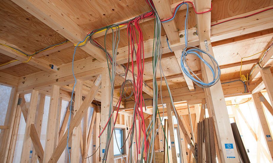 Exposed wooden framing with dangling electrical wires in an unfinished house interior.