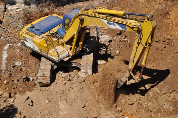 Un escavatore giallo scava in un cantiere sterrato, con la benna che raccoglie la terra.