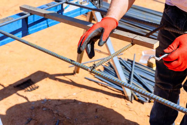 Operaio con guanti rossi che lega barre d'acciaio in un cantiere.