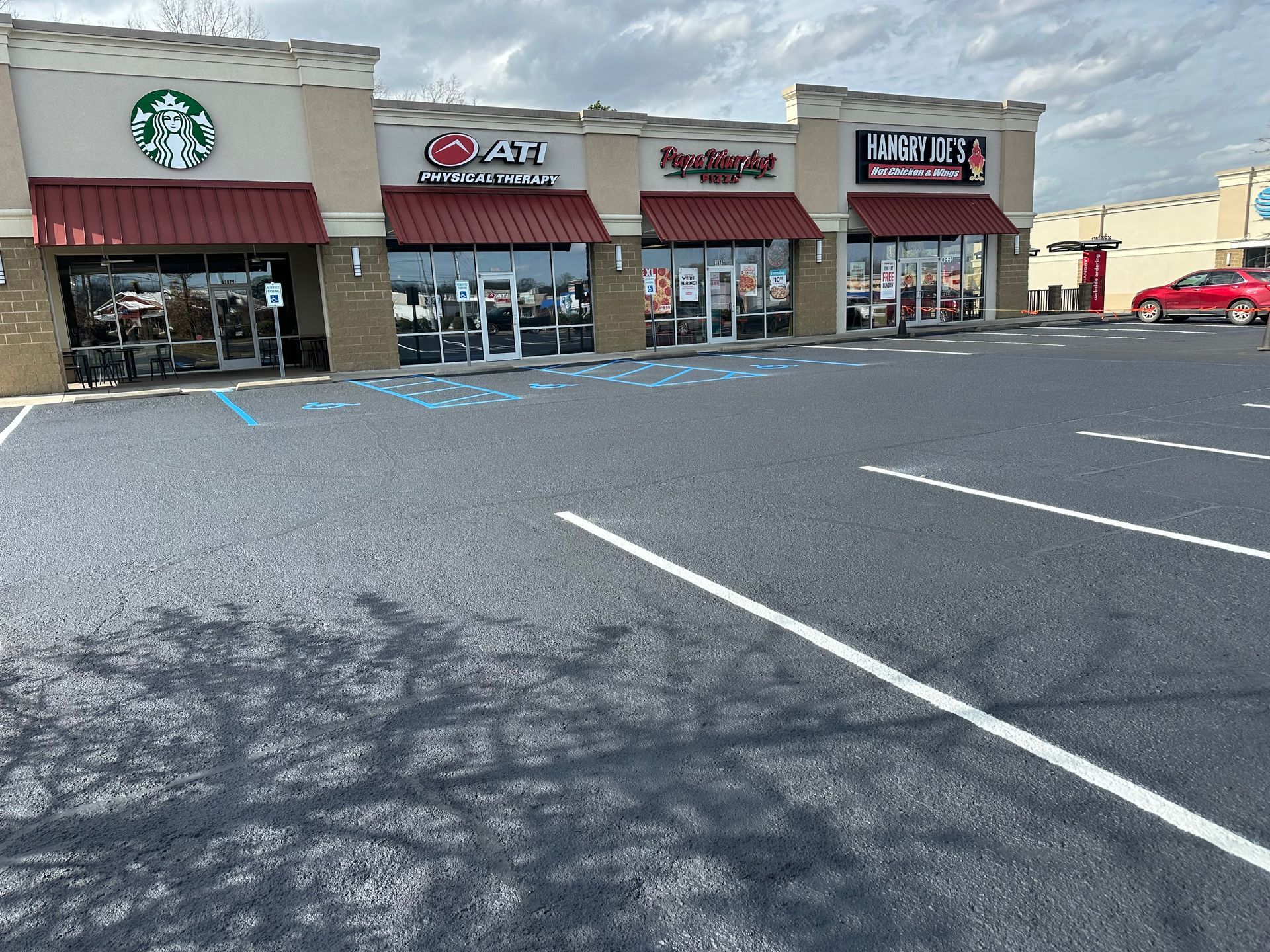 Exterior view of a shopping strip with a Starbucks, Asian restaurant, and other businesses; overcast sky.