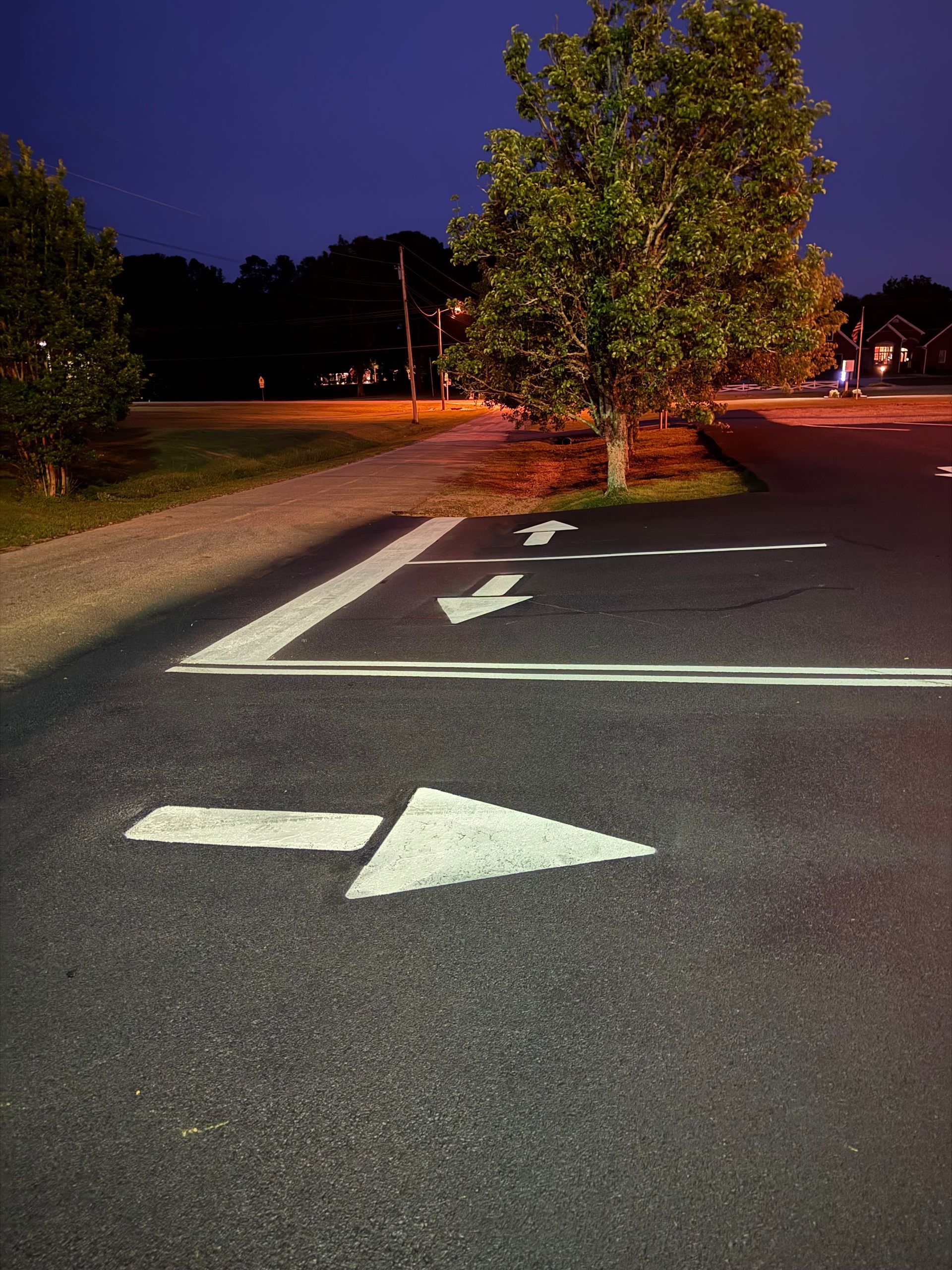 Asphalt parking area with white directional arrows and tree, under dark blue sky.