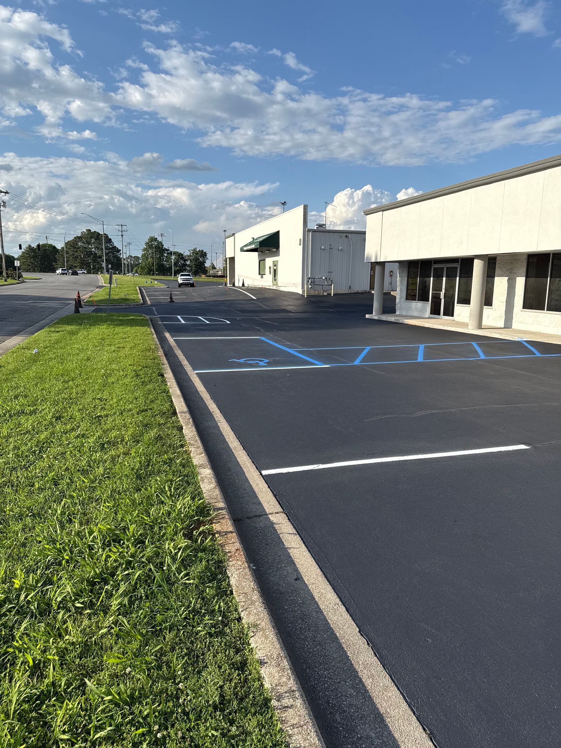Parking lot with handicap spaces, next to a building and grass under a blue sky.