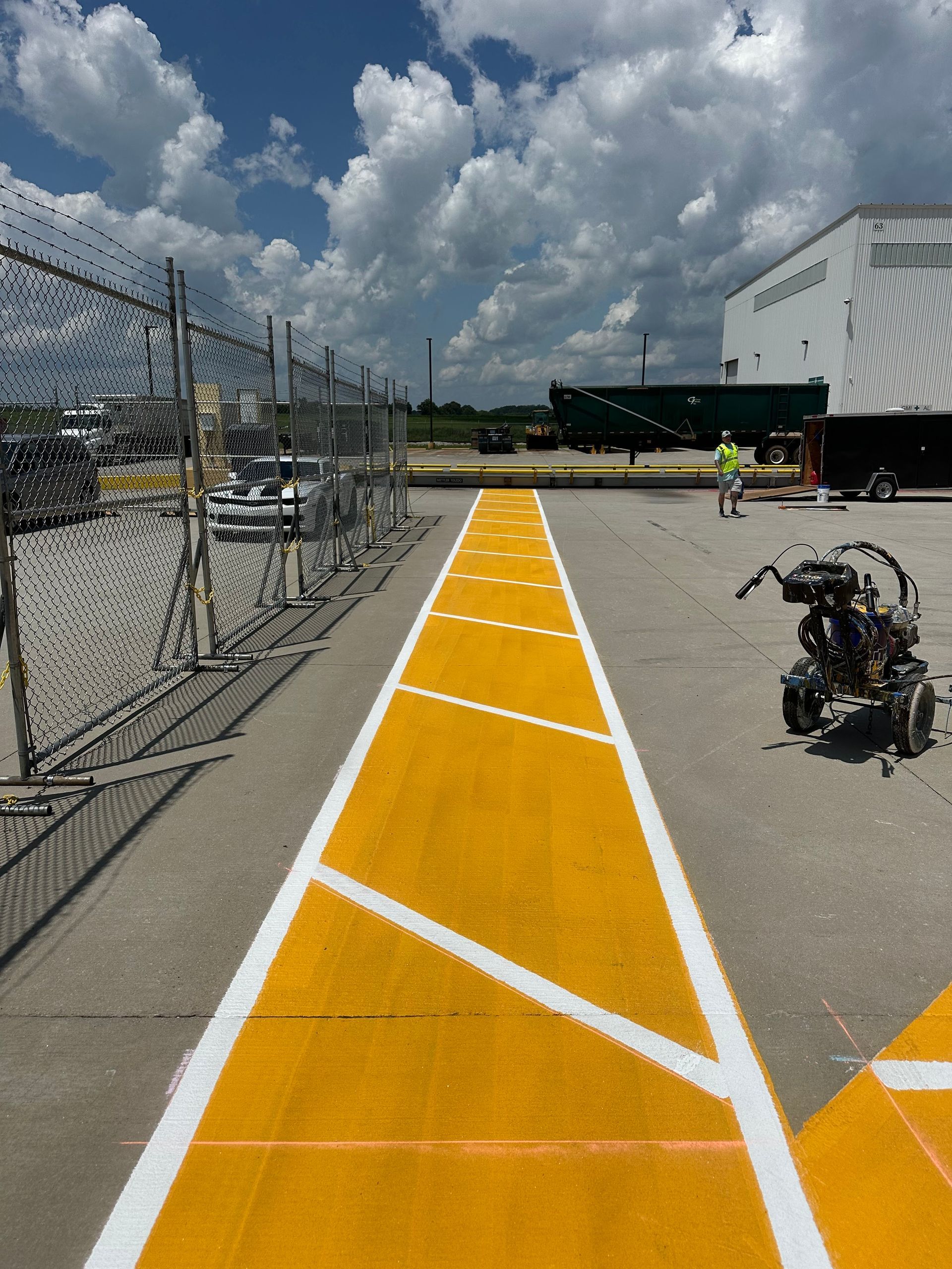 Yellow and white painted markings on asphalt, likely for traffic guidance in an industrial area, with worker.