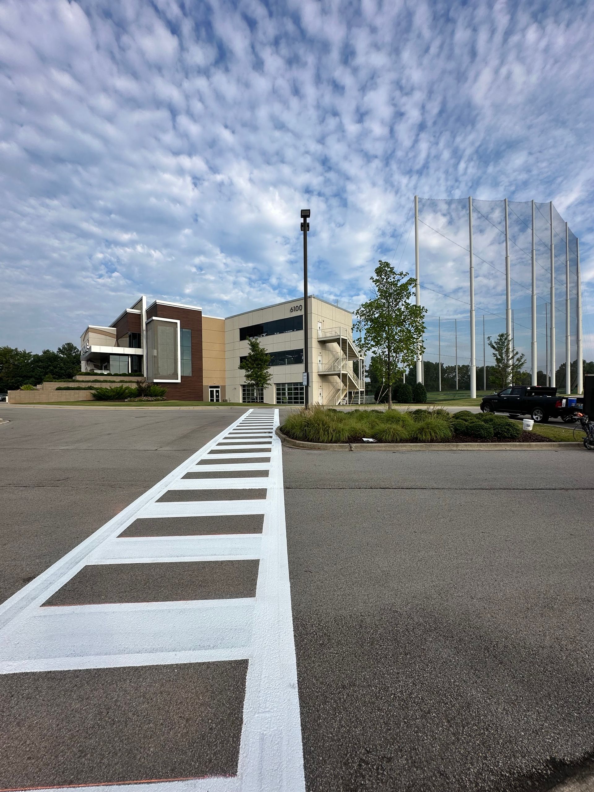 Parking lot with a crosswalk leading to a building. Cloudy sky overhead.