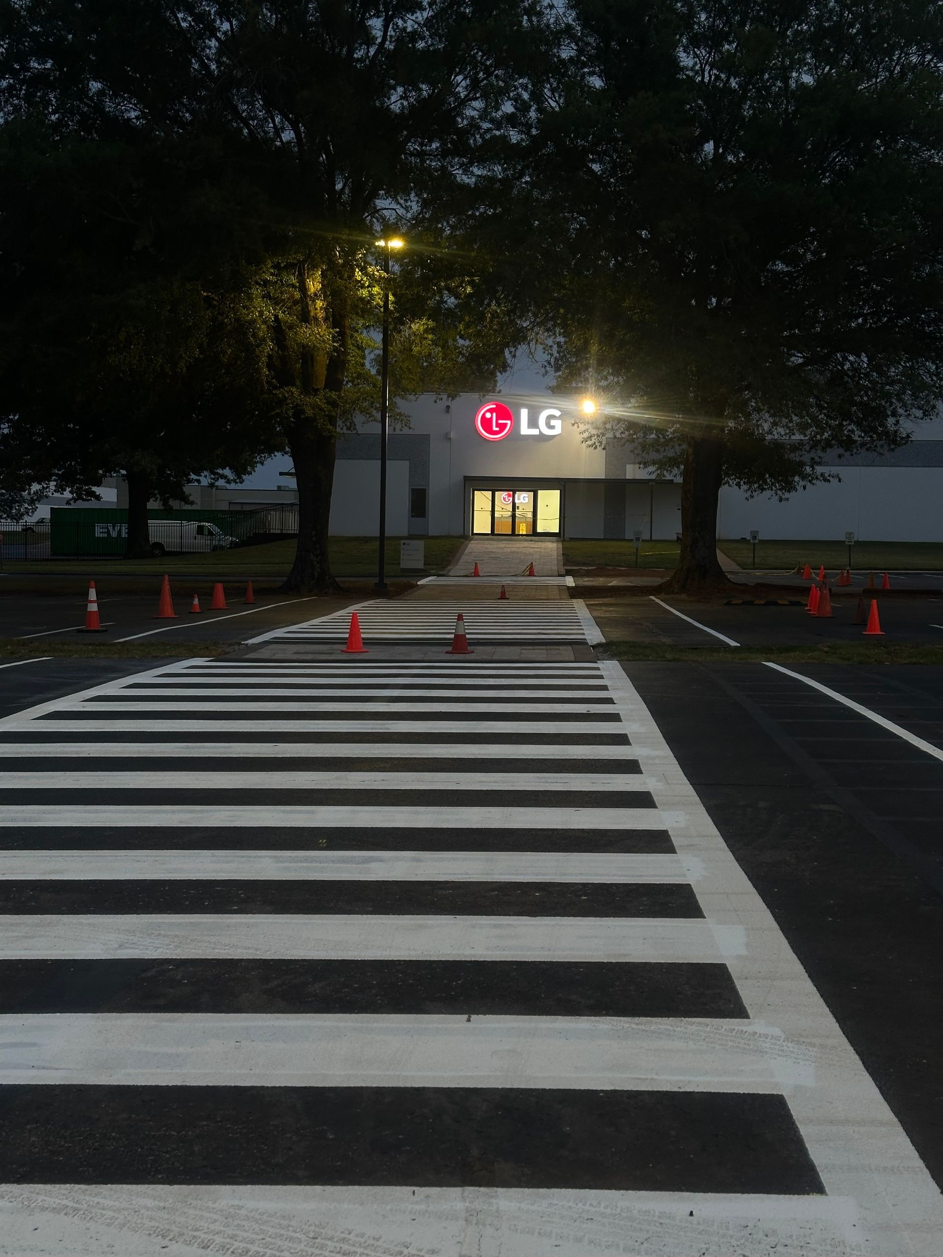 Pedestrian crosswalk leading to an LG building entrance, flanked by trees; night setting.