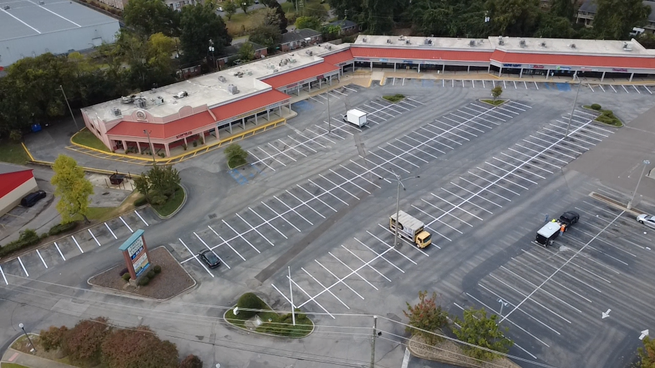 Aerial view of an empty shopping center parking lot. The red-roofed building has several storefronts.