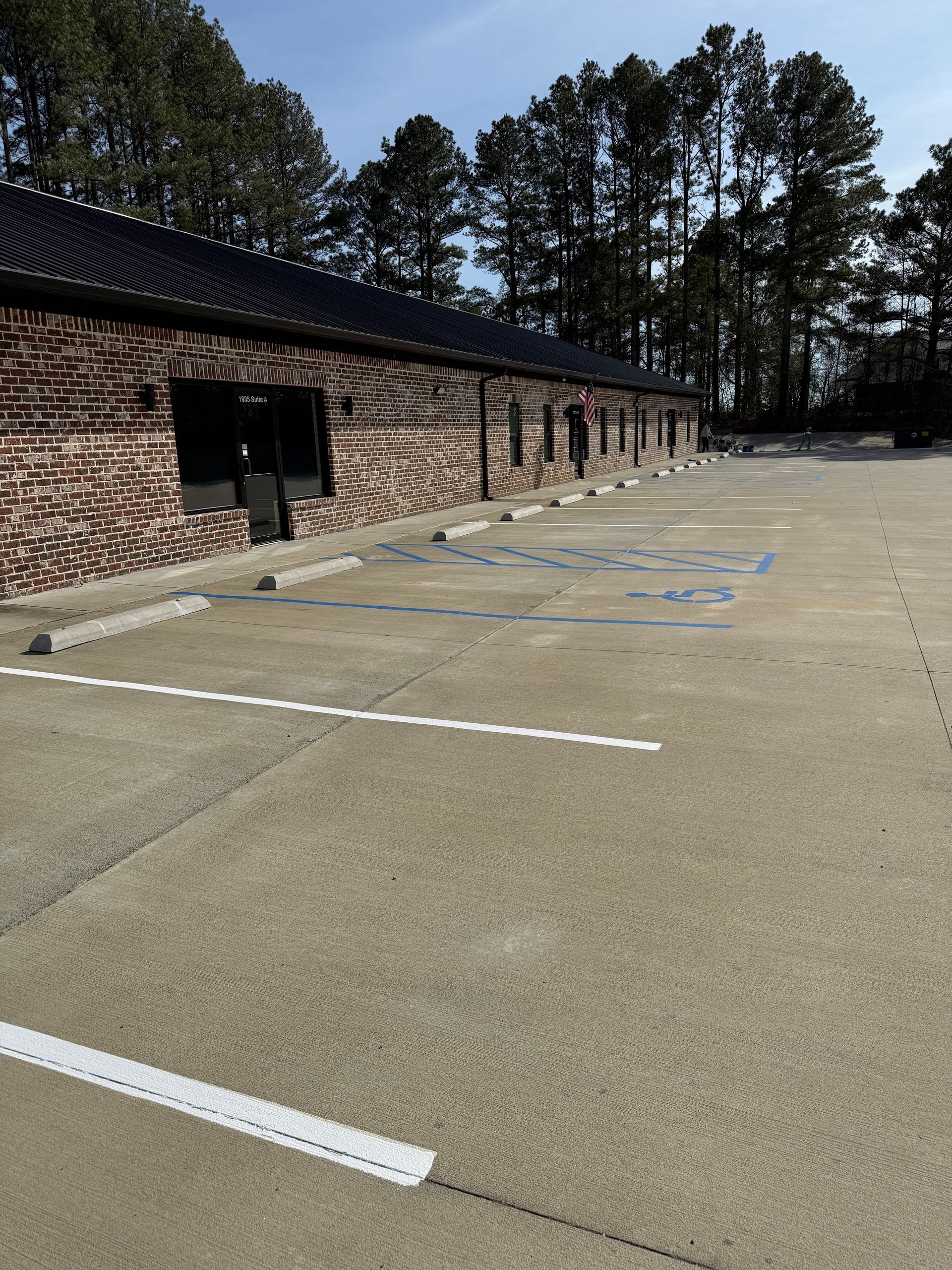 Brick building with parking spaces and trees in the background on a sunny day.