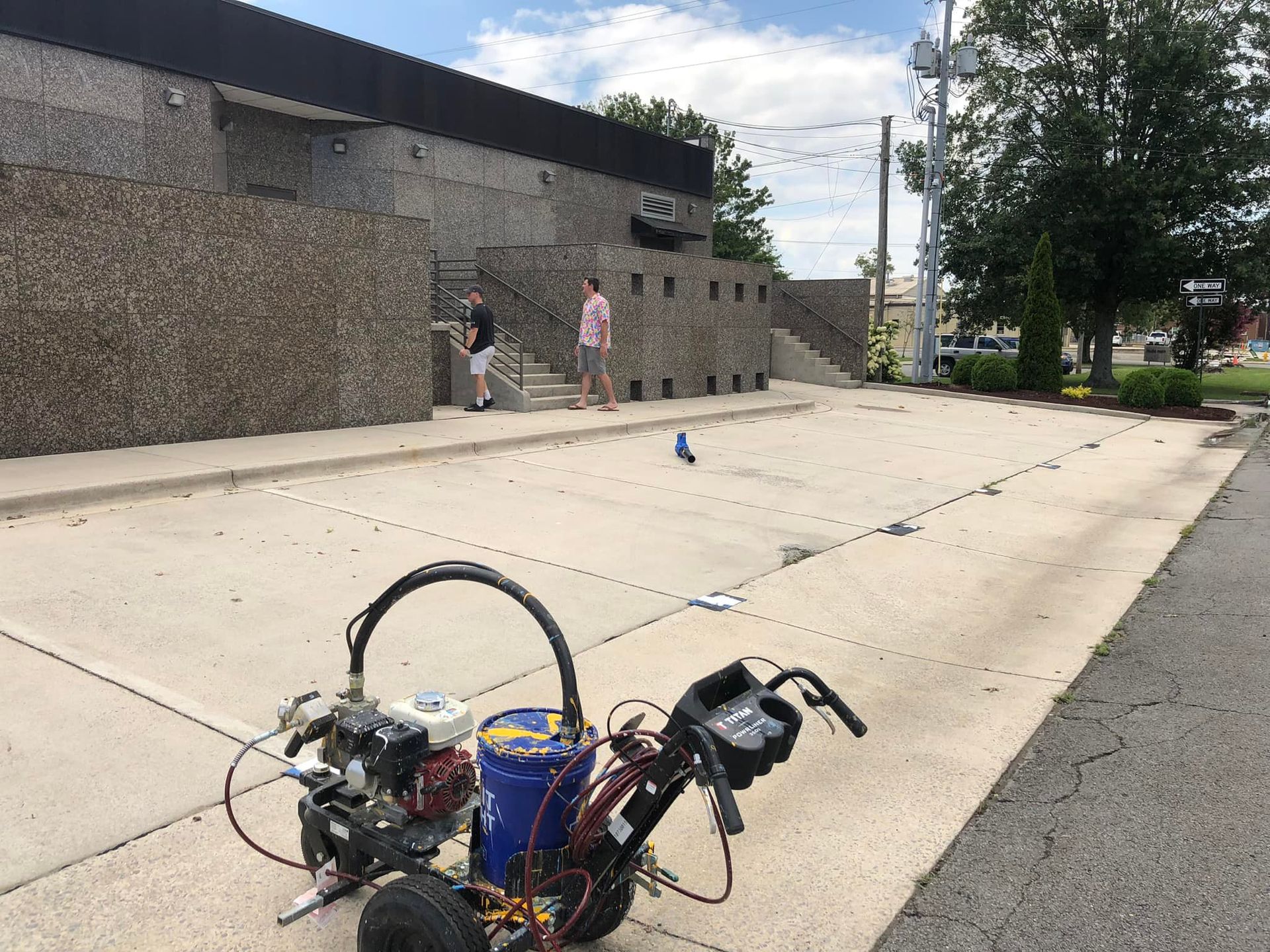 A parking lot striping machine with two people near a building.