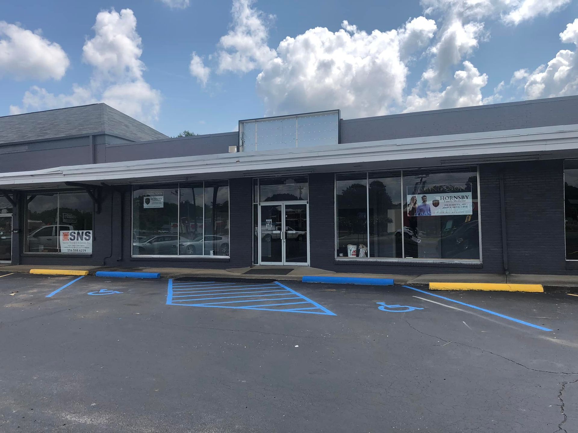 Exterior of a dark gray comm.building with large windows and a central entrance, accessible parking spaces marked in blue.
