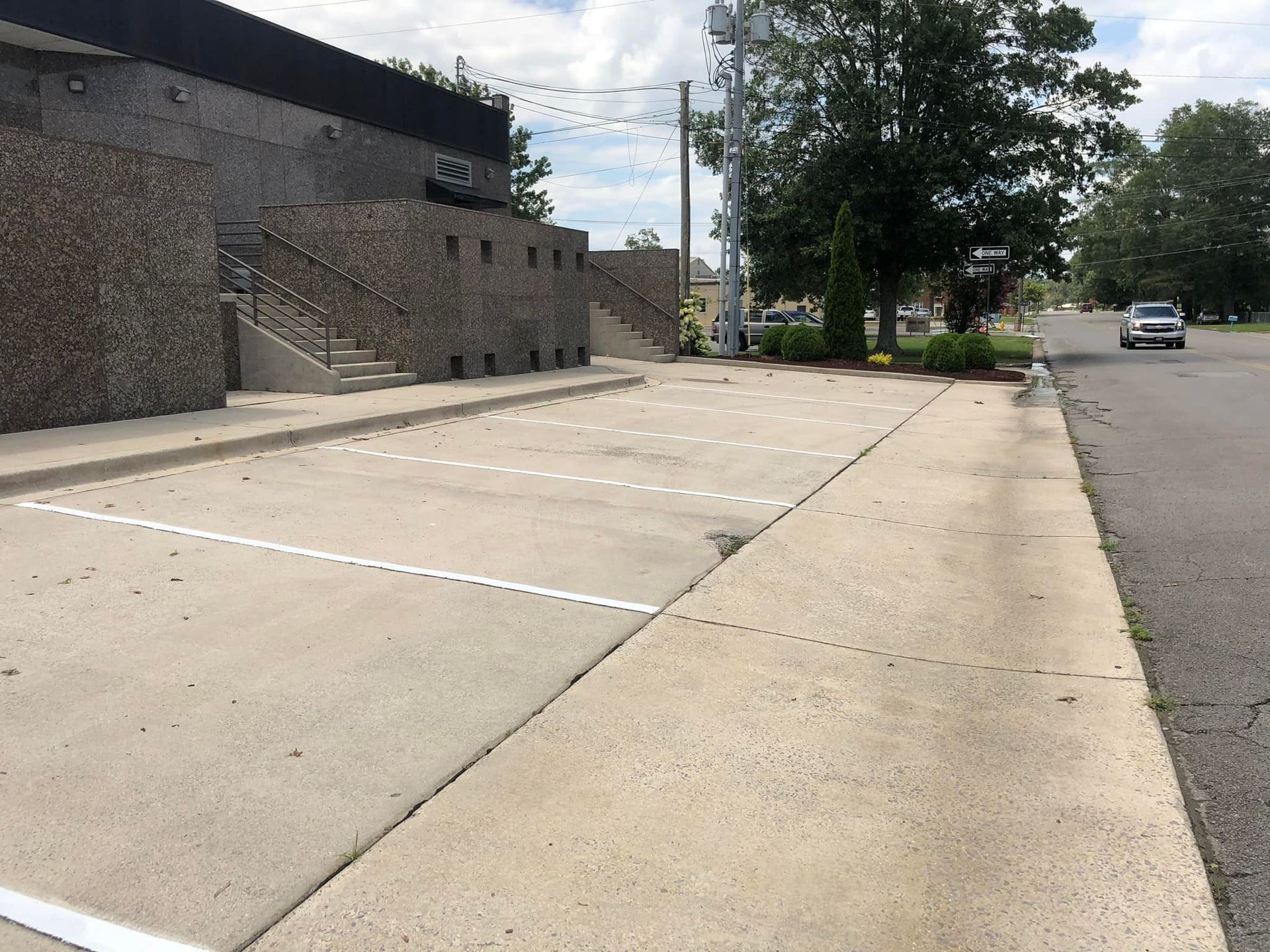 Concrete parking spaces next to a building and sidewalk, a car drives on a street.