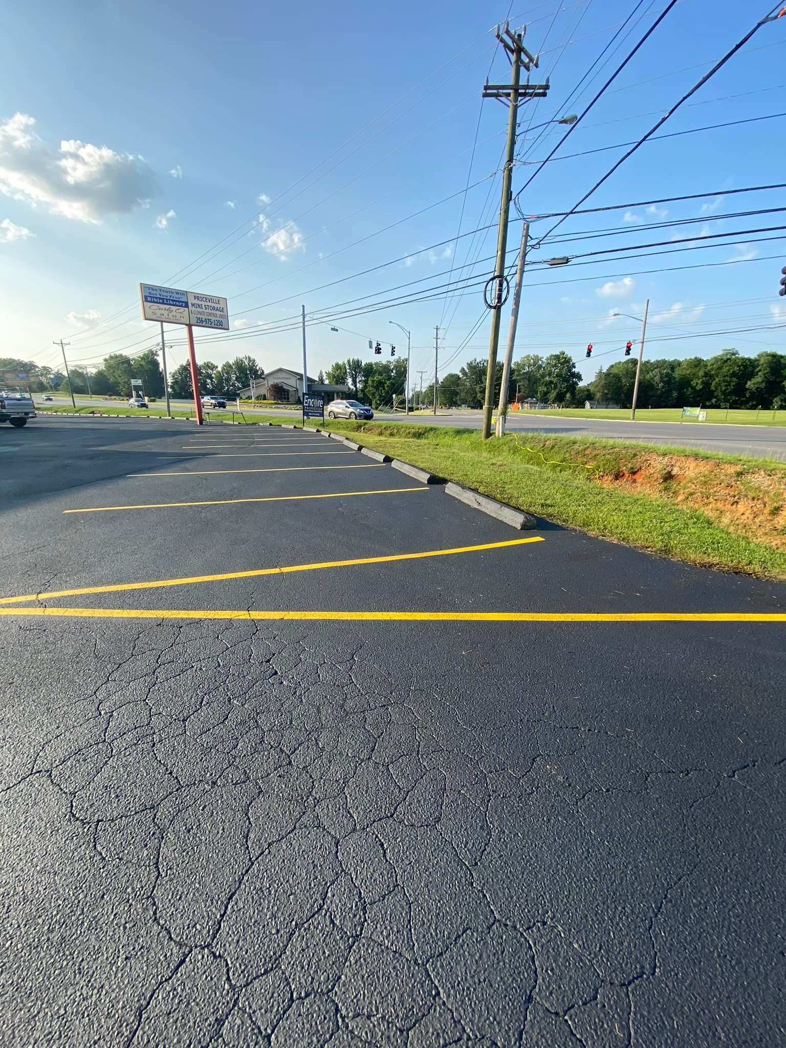 Newly paved asphalt road with yellow lines, power lines, and a sign in the background.