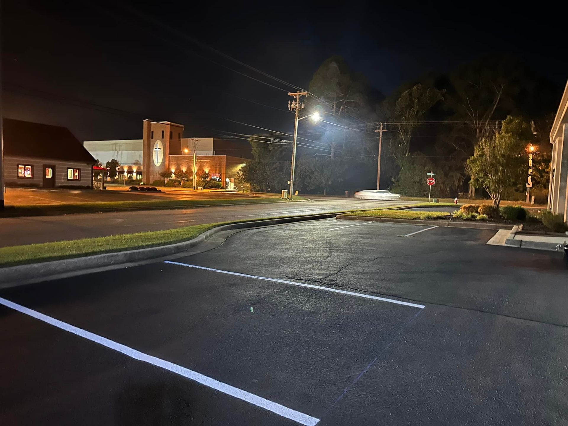 Nighttime street scene with illuminated buildings, road, and power lines.