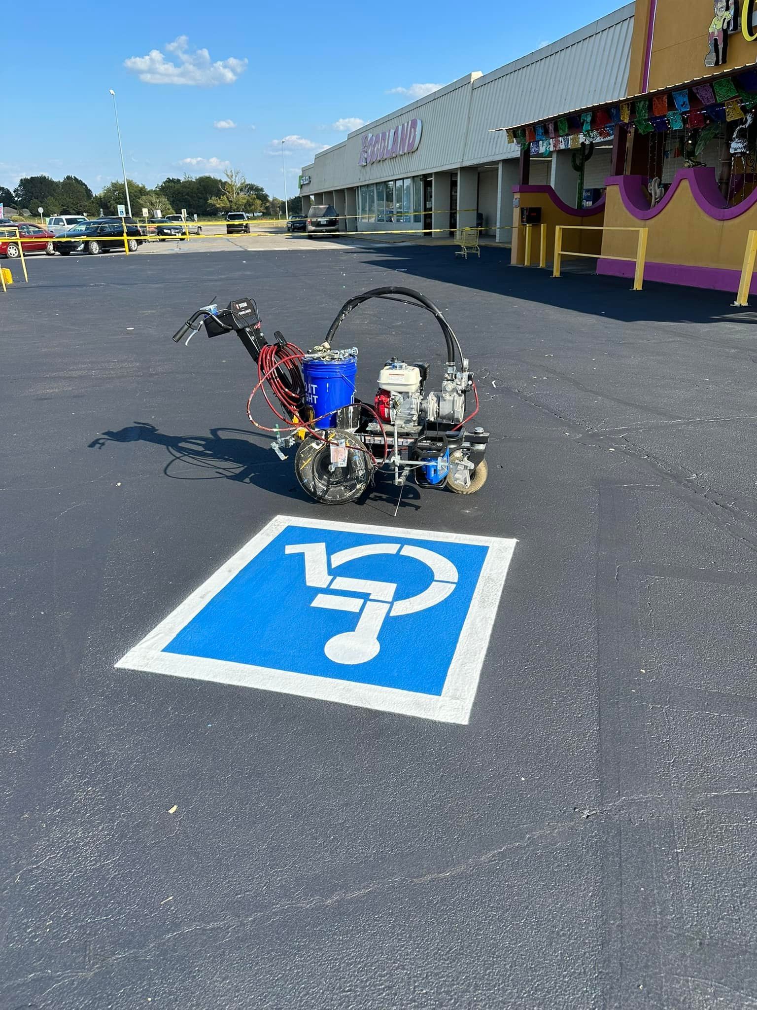 Handicap parking space being painted in blue with stencil; paint machine in parking lot.
