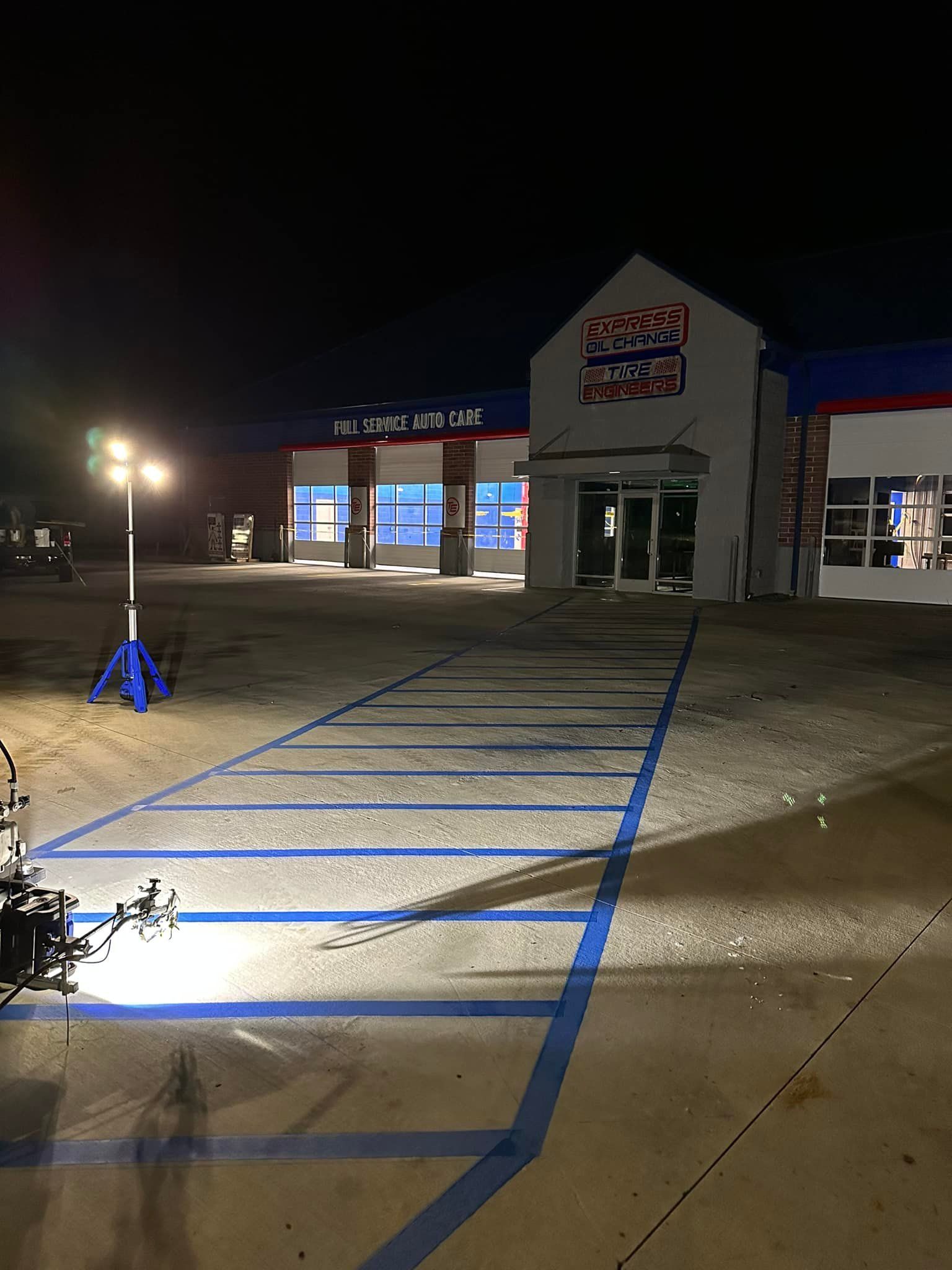 Nighttime exterior of a business, illuminated by a light. Blue parking space lines and a sign are visible.