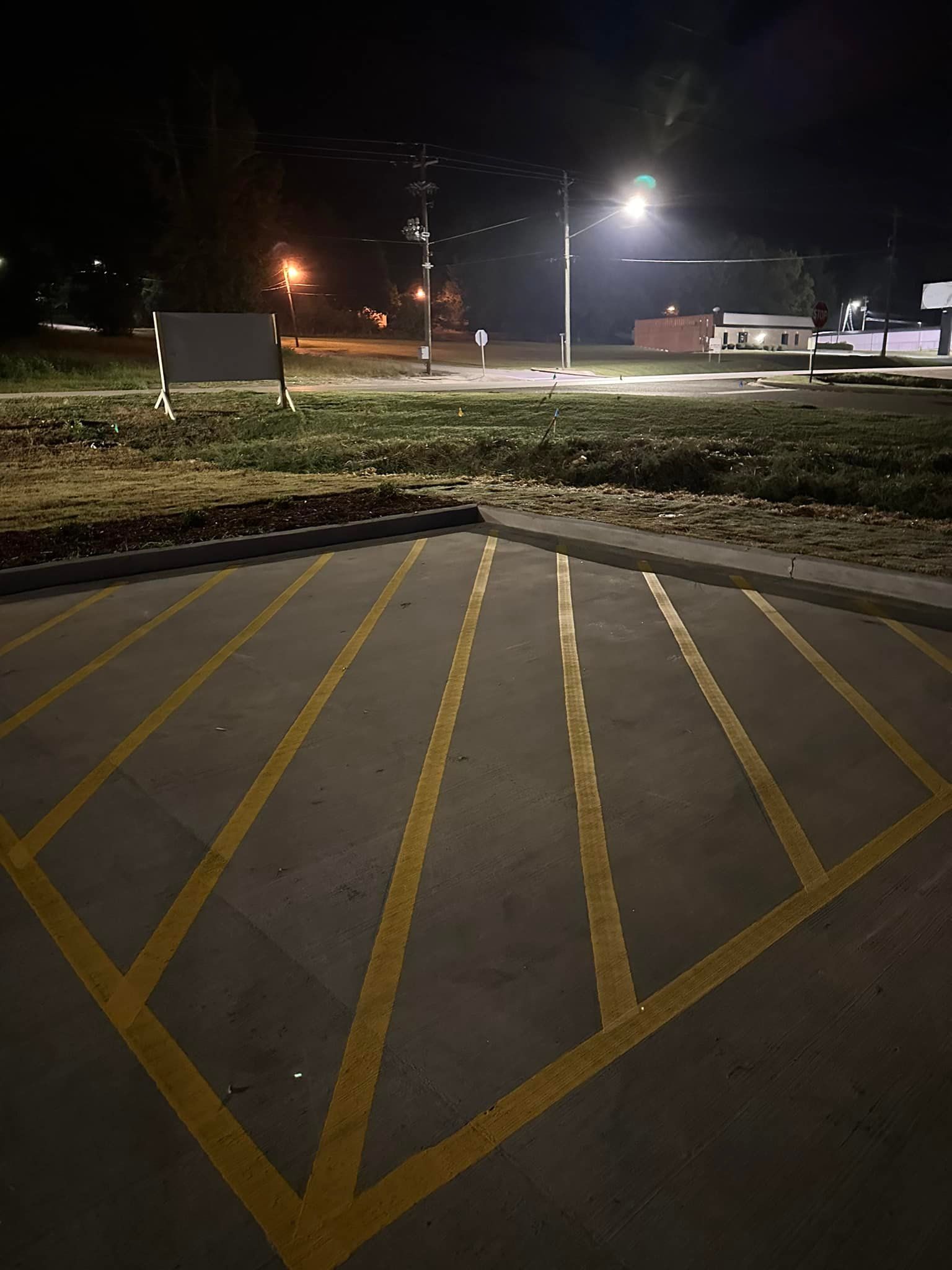 Parking lot at night with yellow parking lines radiating out from a point. Buildings and streetlights in the background.
