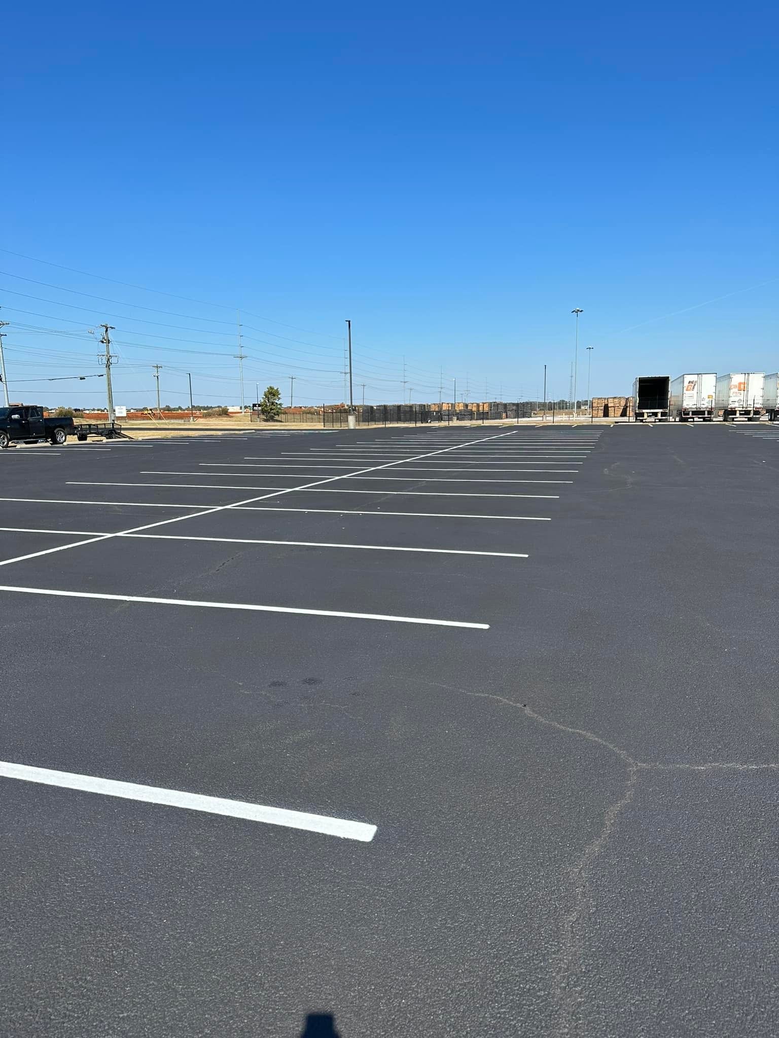 Empty asphalt parking lot with white painted lines under a clear blue sky.