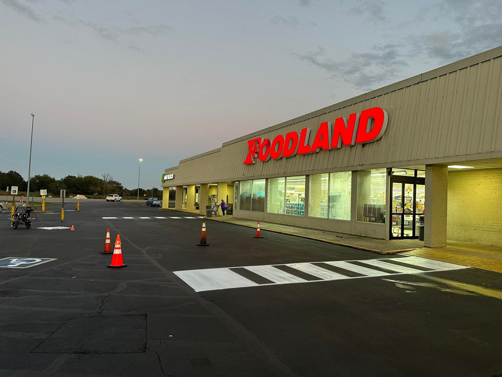 Foodland grocery store exterior with red sign, crosswalk, and orange traffic cones.