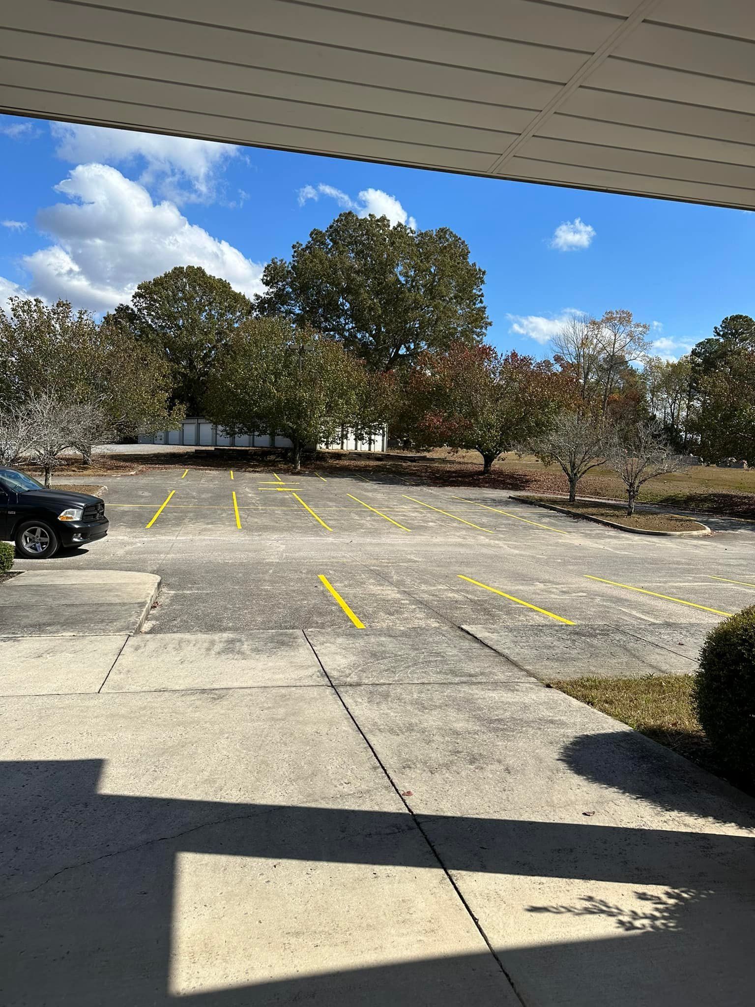 Concrete parking lot with yellow painted lines and trees in the background under a blue sky.