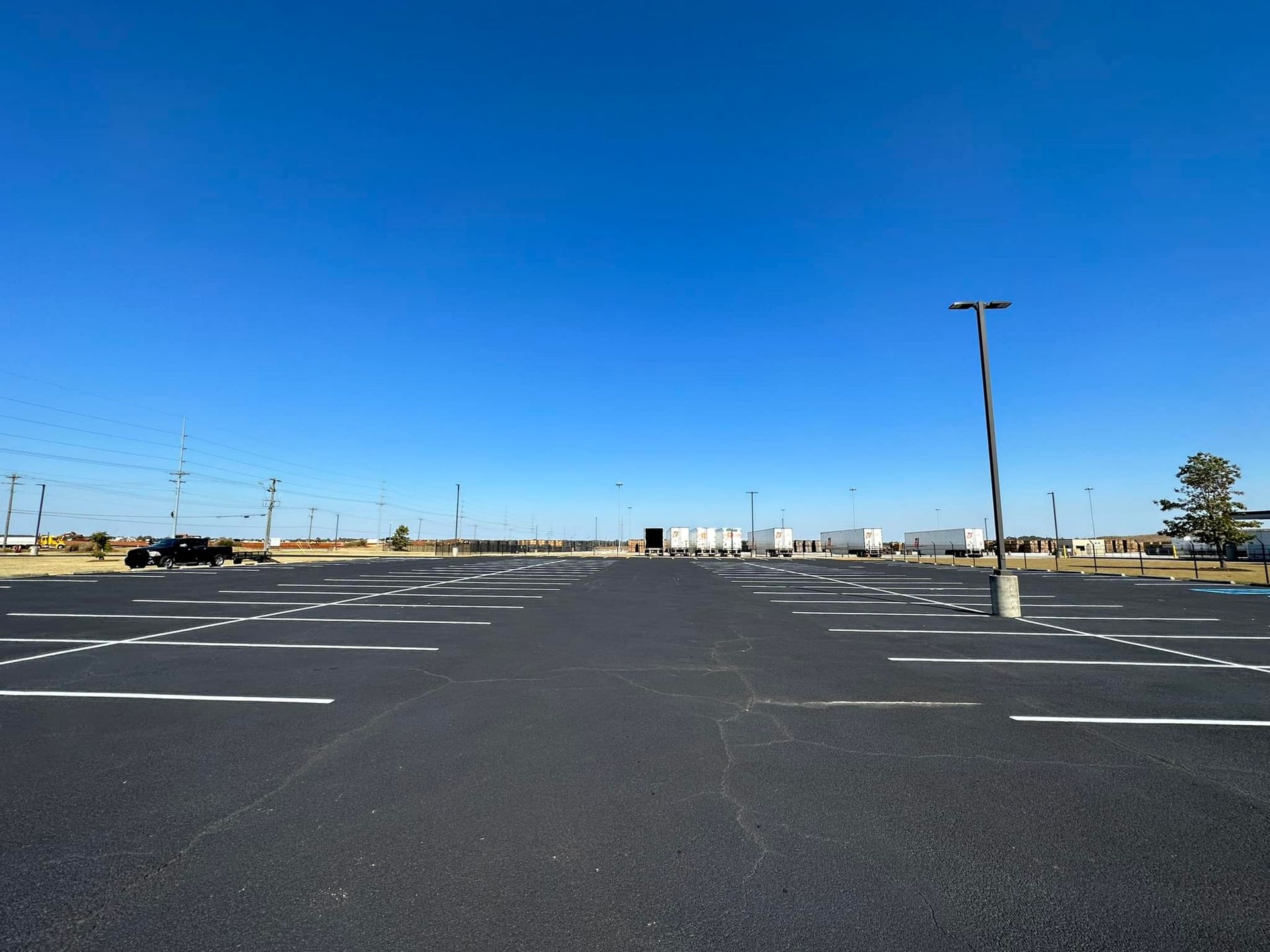Empty asphalt parking lot under a clear blue sky, with white parking space lines.