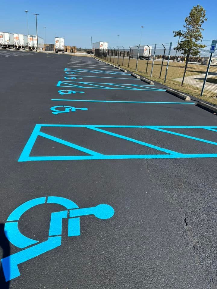Blue painted handicap parking spaces on dark asphalt with a line of semi-trucks in the background.
