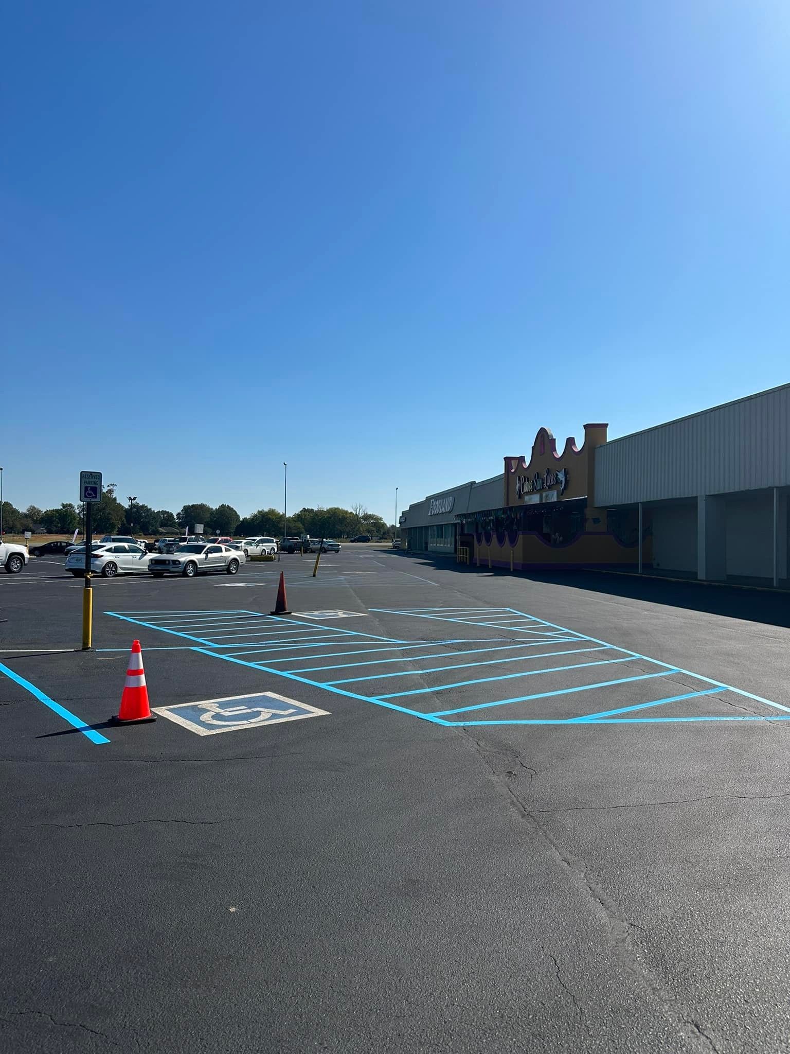 Empty parking lot with blue painted spaces, orange cone, and a blue sky.