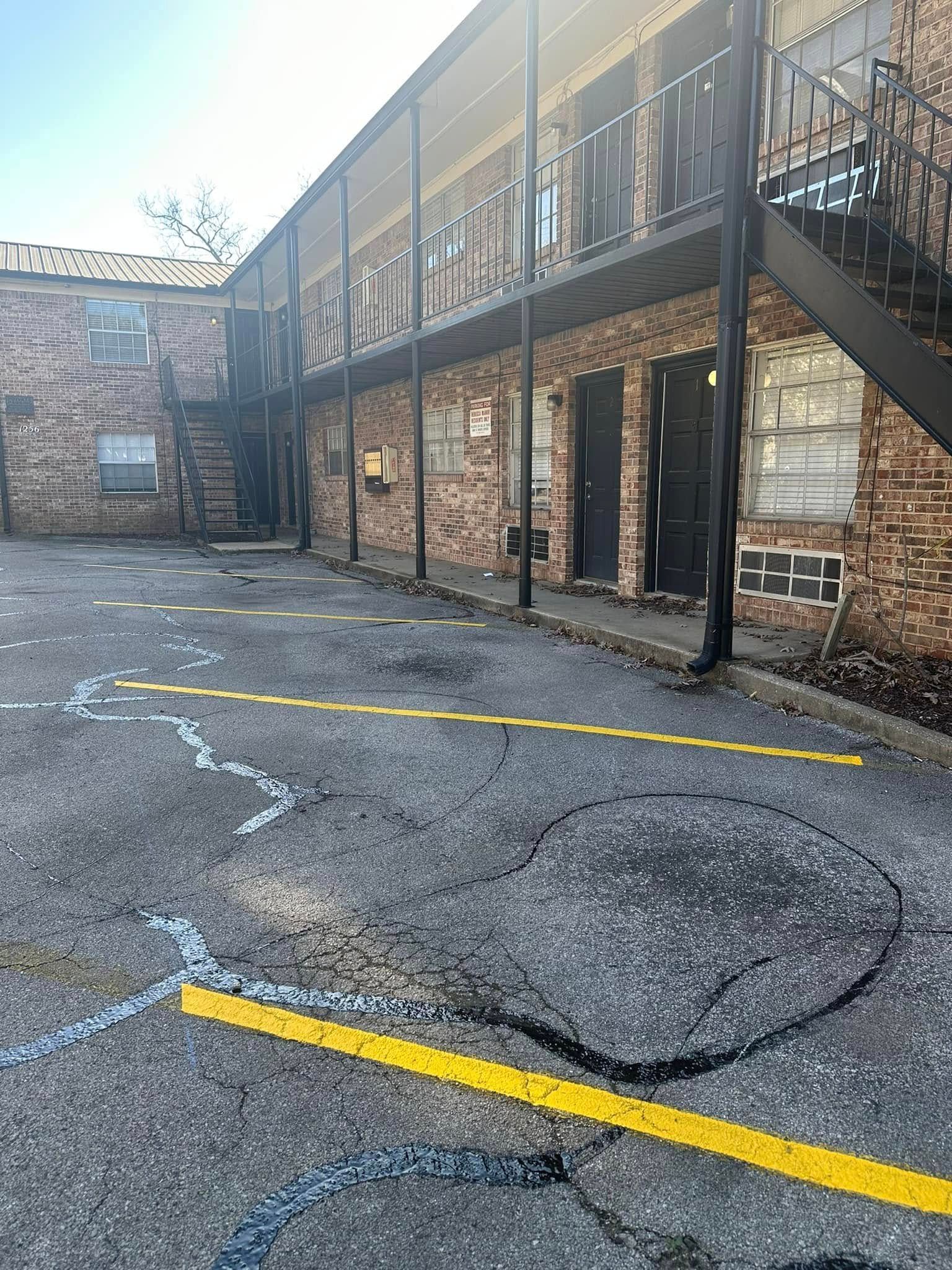 Apartment building with cracked asphalt parking lot, yellow painted lines, and metal stairwells.