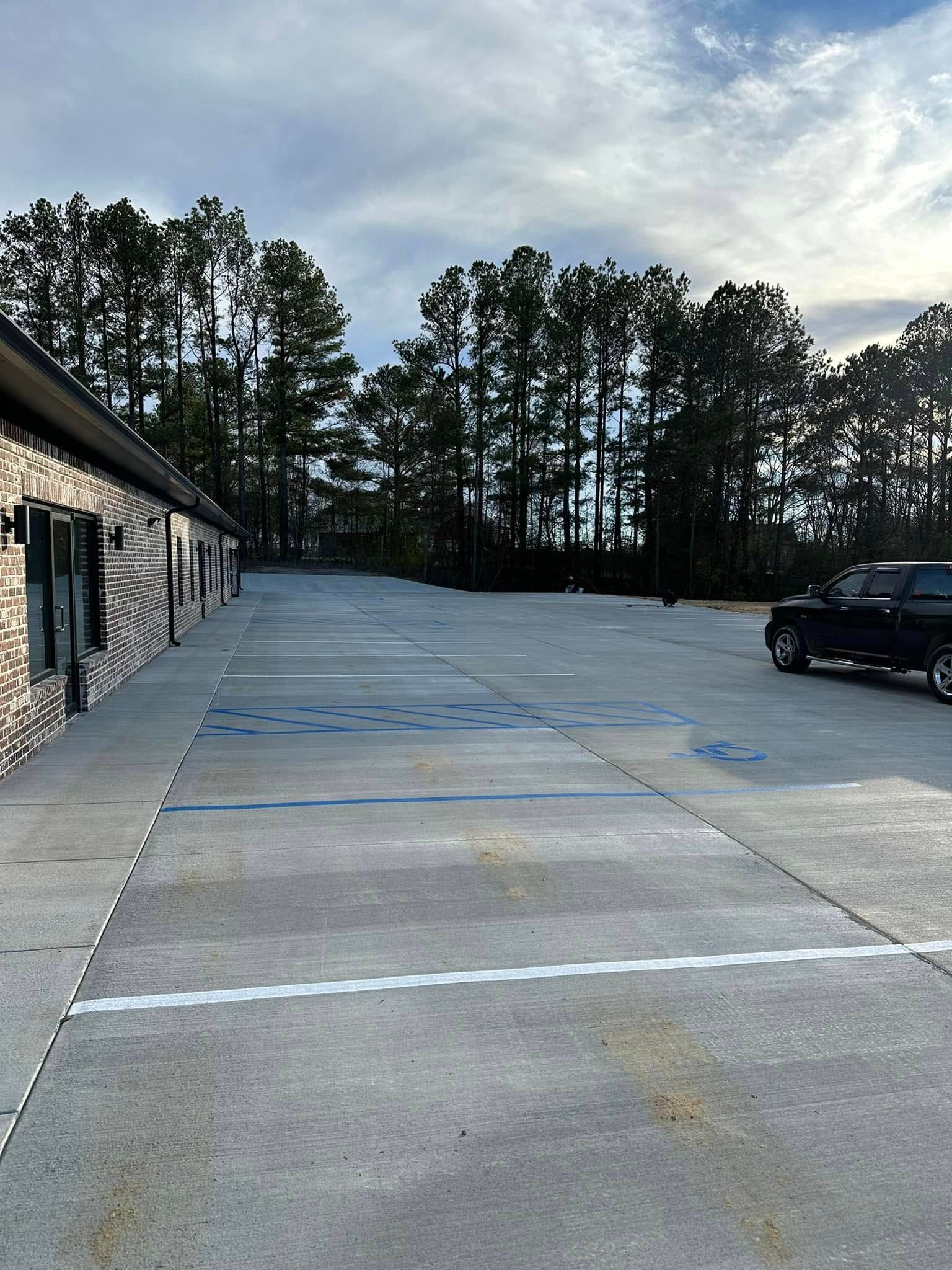 Parking lot with a building on the left and trees in the background, a truck is parked in the lot.