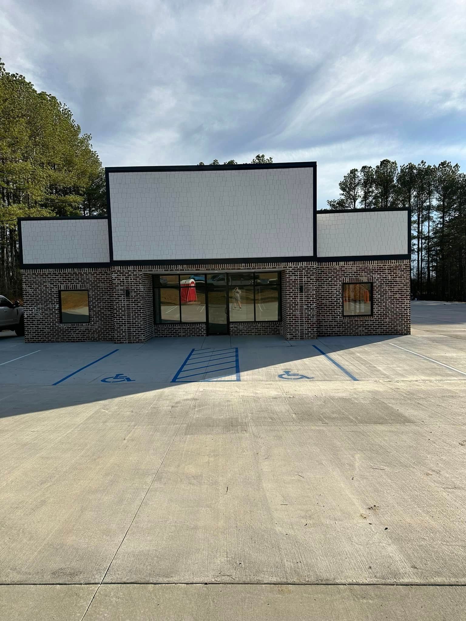 Exterior of a brick commercial building with a blank sign. Windows, a glass door, and parking lot in front.