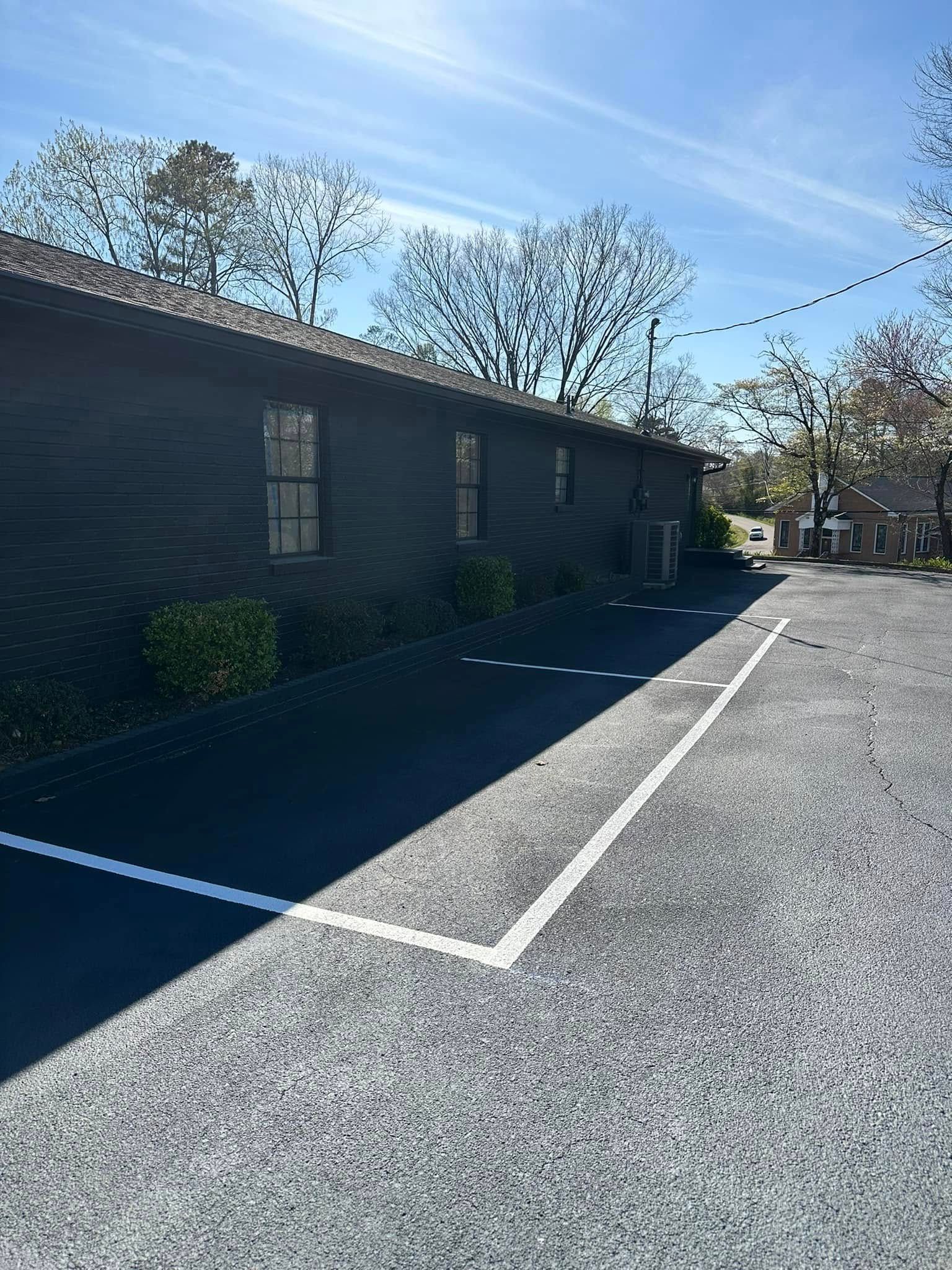 Black building with parking spaces marked by white lines on asphalt, sunny day.