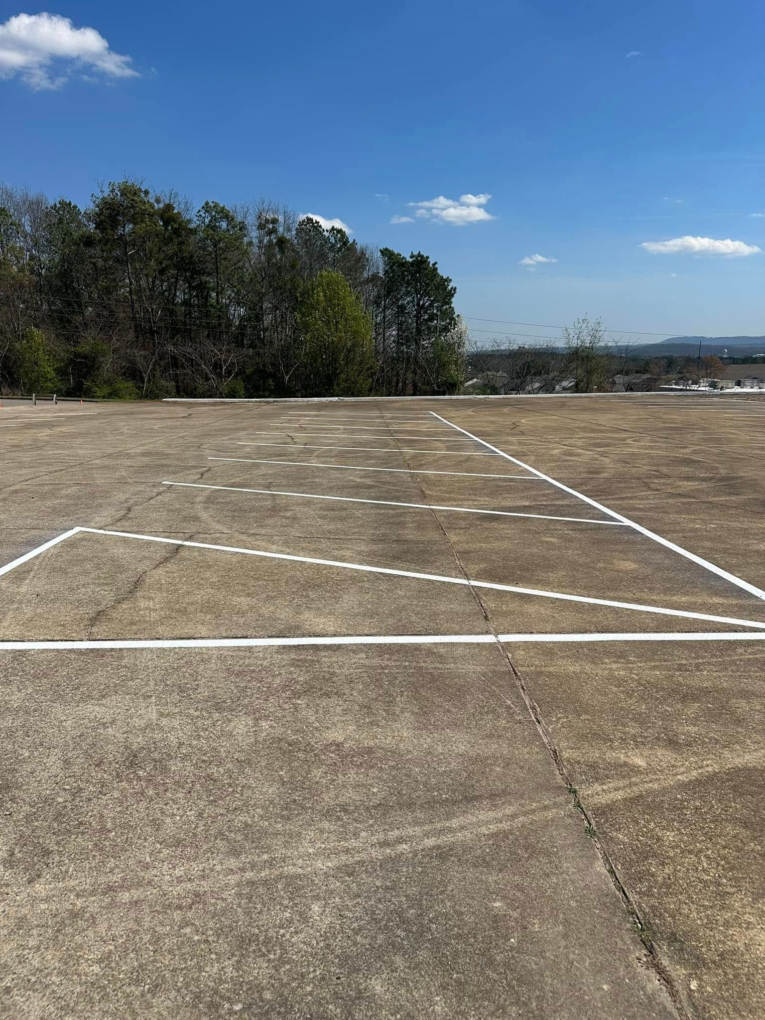 Concrete surface with white lines and dotted circles, trees in the background, blue sky.