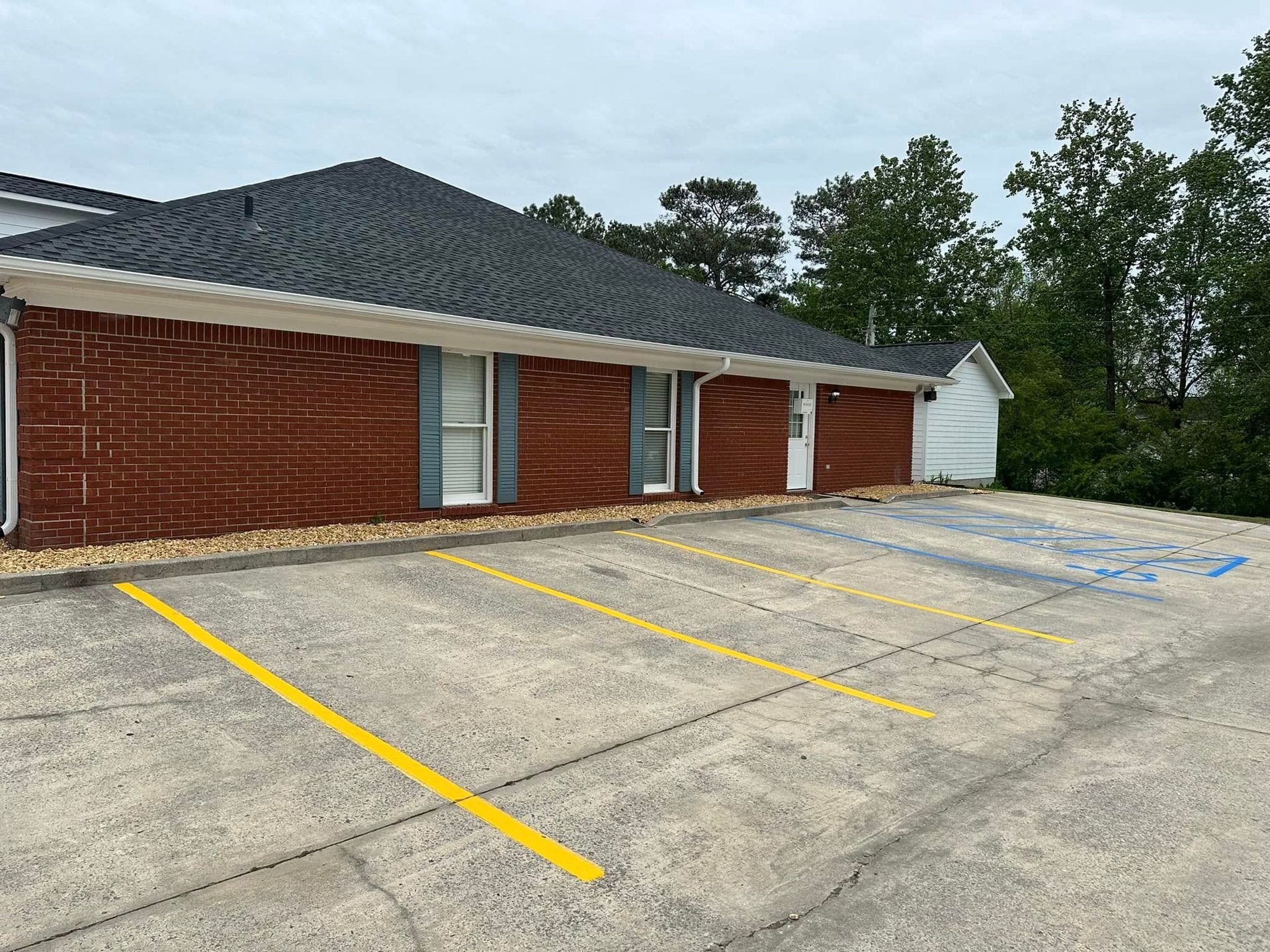Exterior view of a red brick building with a parking lot. Blue handicap parking space visible.
