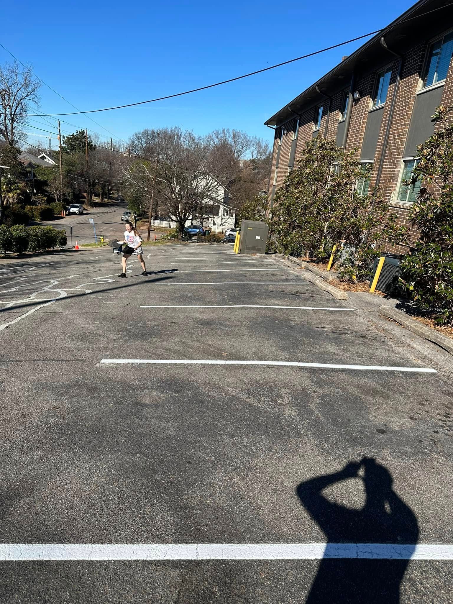 A person running in a parking lot. Buildings and trees in the background under a blue sky.