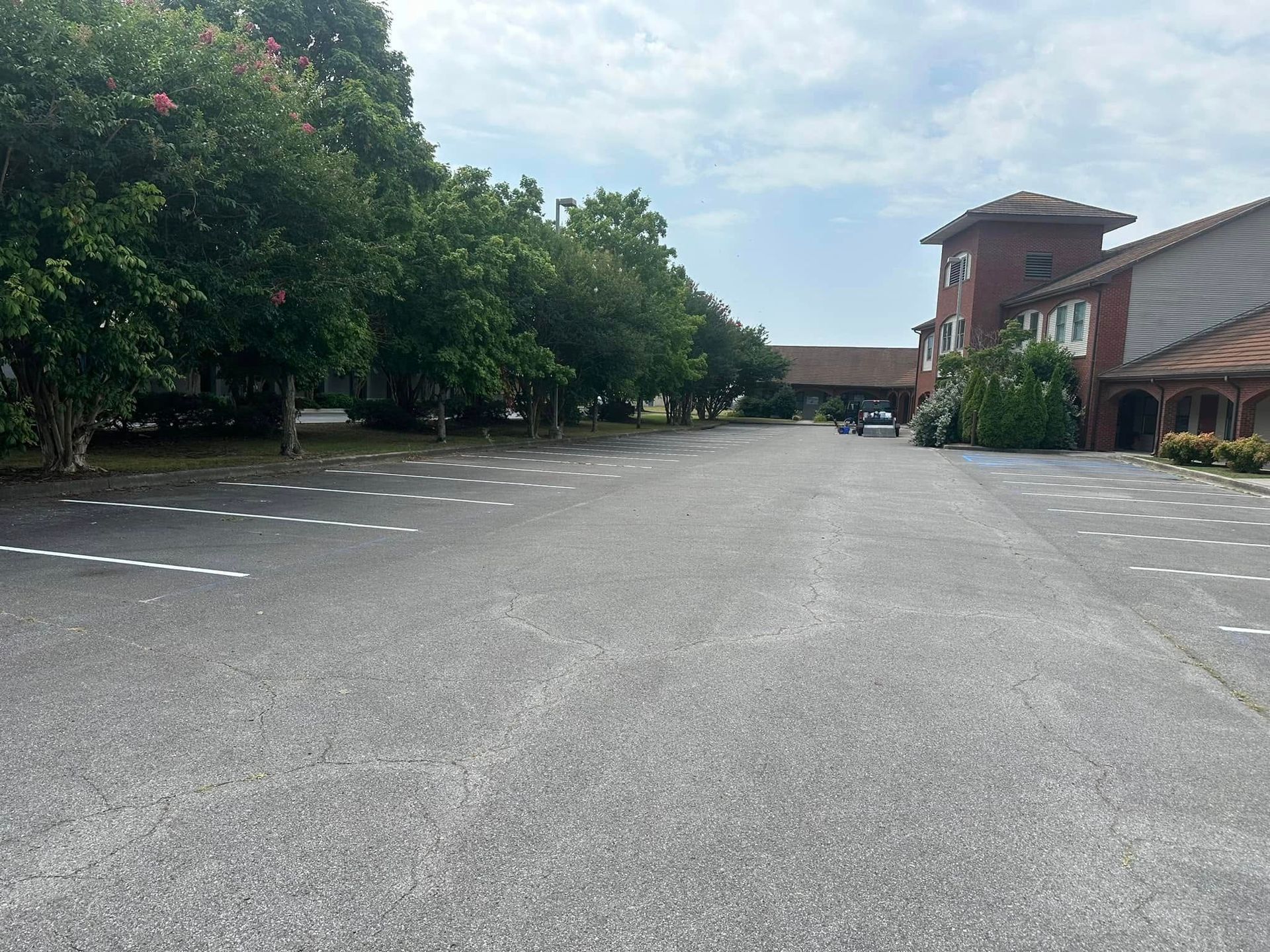 Empty parking lot with trees and a red brick building under a cloudy sky.