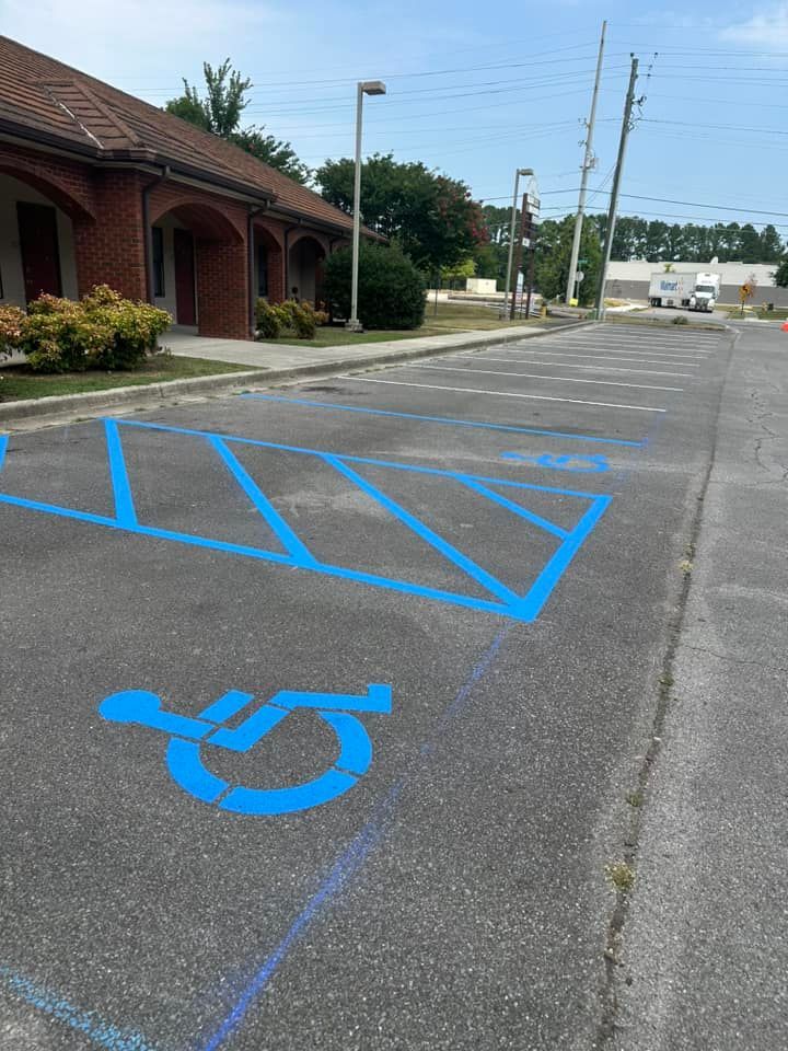 Blue painted accessible parking spaces in a parking lot. Building and utility poles in the background.