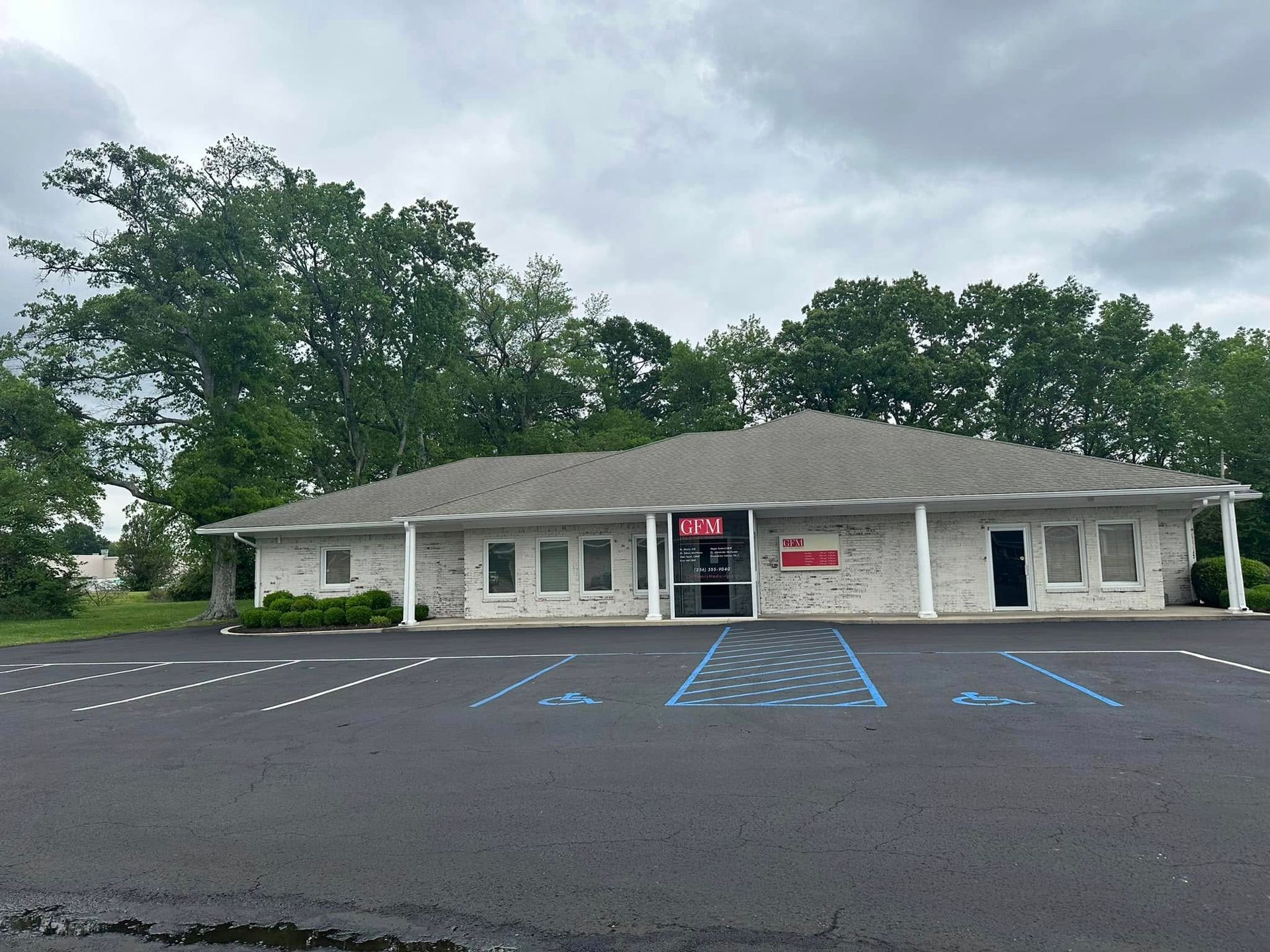 Exterior of a one-story brick building with several windows and a parking lot on a cloudy day.